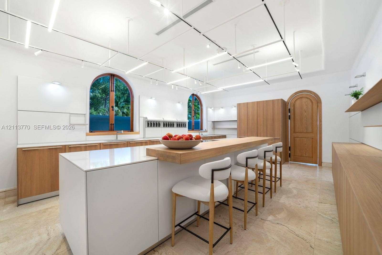 387 Ocean Boulevard, Golden Beach, Golden Beach, FL 33160 Kitchen featuring flat-panel cabinetry with wood-finish and matte-white surfaces, central island with an integrated wood-grain breakfast bar, arched windows, stone-tile flooring, and grid-pattern overhead track lighting