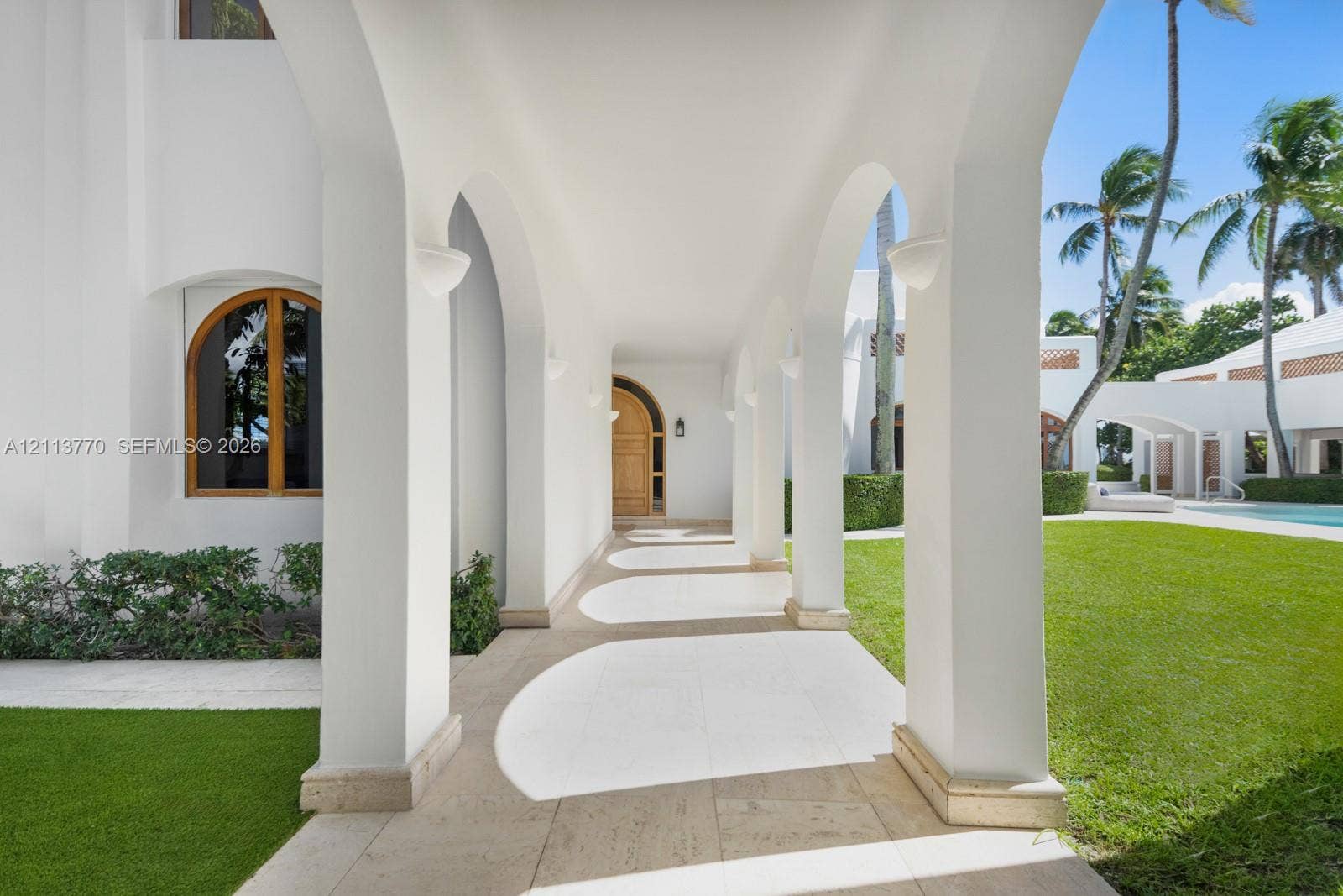 387 Ocean Boulevard, Golden Beach, Golden Beach, FL 33160 Covered arcade featuring rhythmic structural arches, natural stone flooring, and built-in wall-mounted sconces