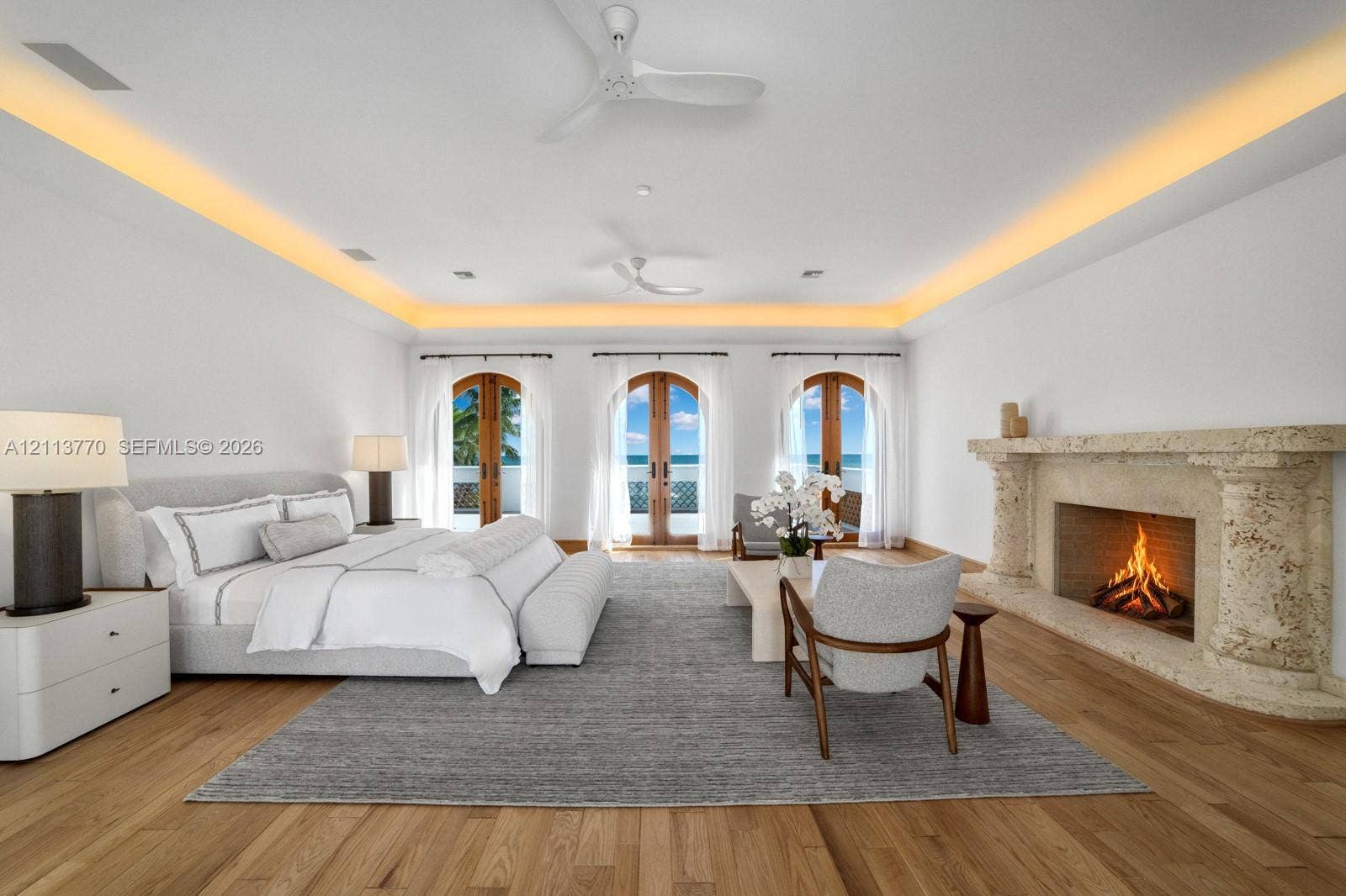 387 Ocean Boulevard, Golden Beach, Golden Beach, FL 33160 Spacious room featuring wood-finish flooring, recessed tray ceiling lighting, dual white ceiling fans, and an ornate, textured stone fireplace surround with arched French doors