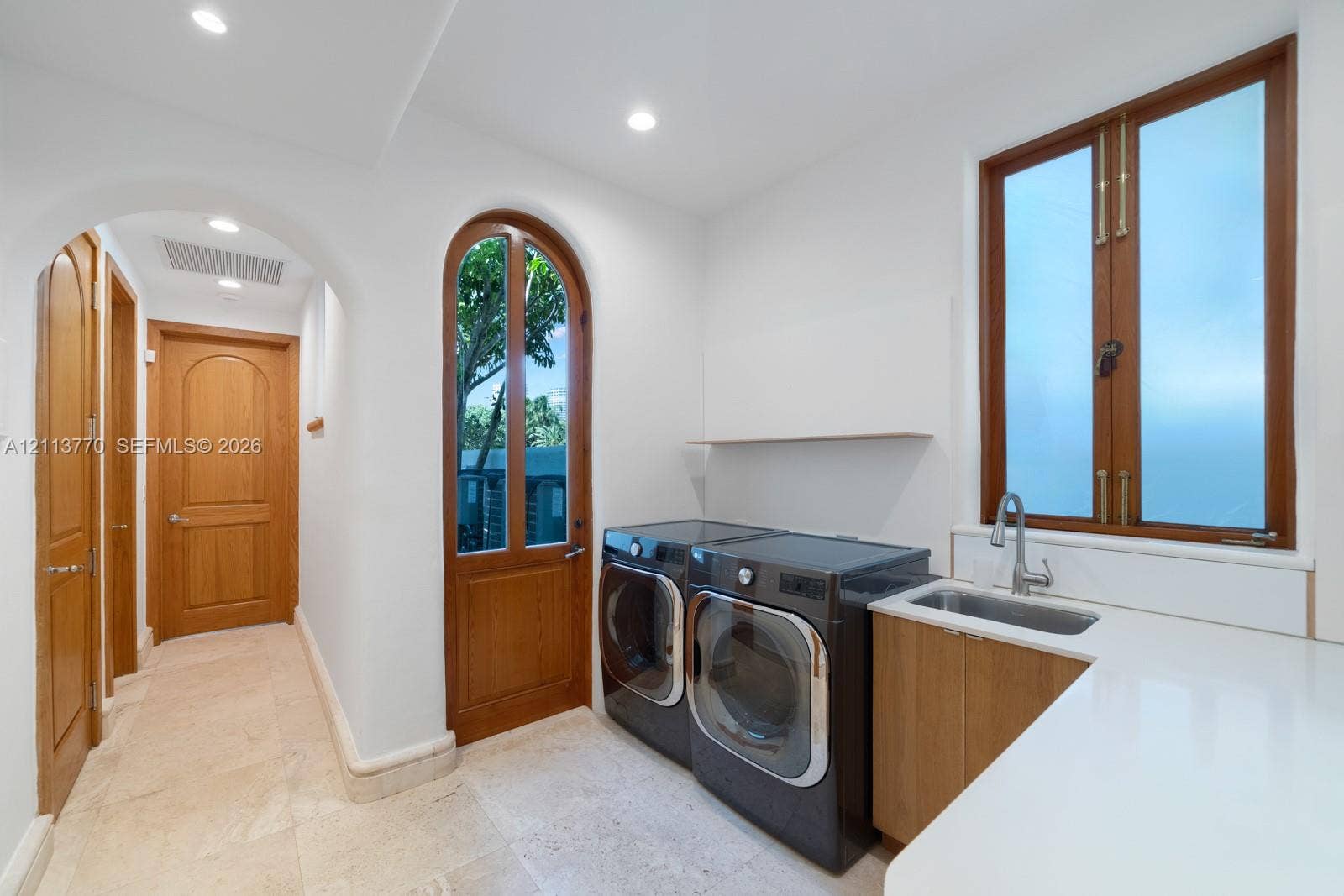 387 Ocean Boulevard, Golden Beach, Golden Beach, FL 33160 Laundry area featuring stone tile flooring, an arched glass-paneled door, custom wood cabinetry with a sink, and a solid surface countertop