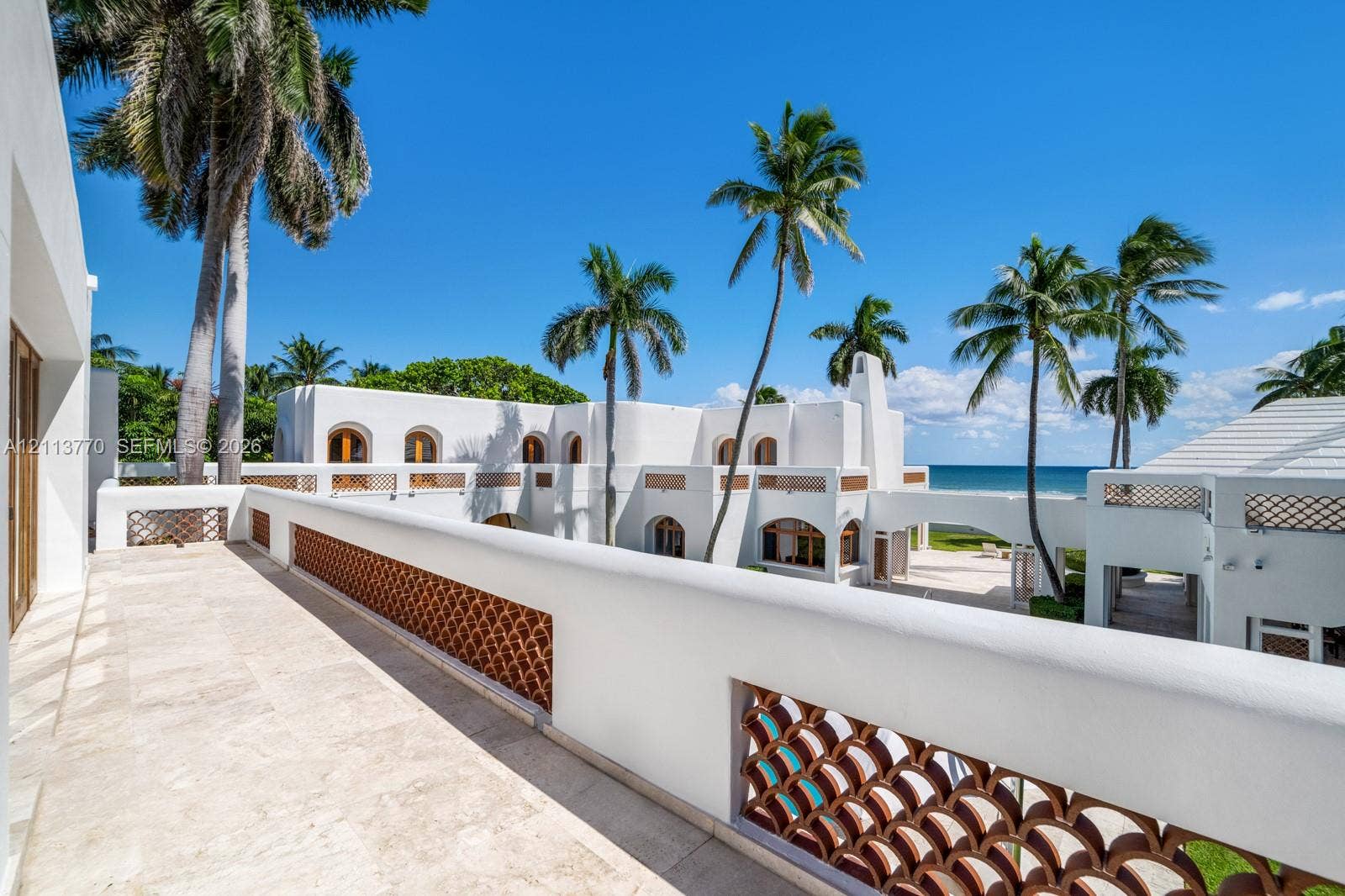 387 Ocean Boulevard, Golden Beach, Golden Beach, FL 33160 Second-story stone terrace featuring decorative terracotta latticework railings, stucco exterior walls, arched architectural detailing, and ocean surroundings