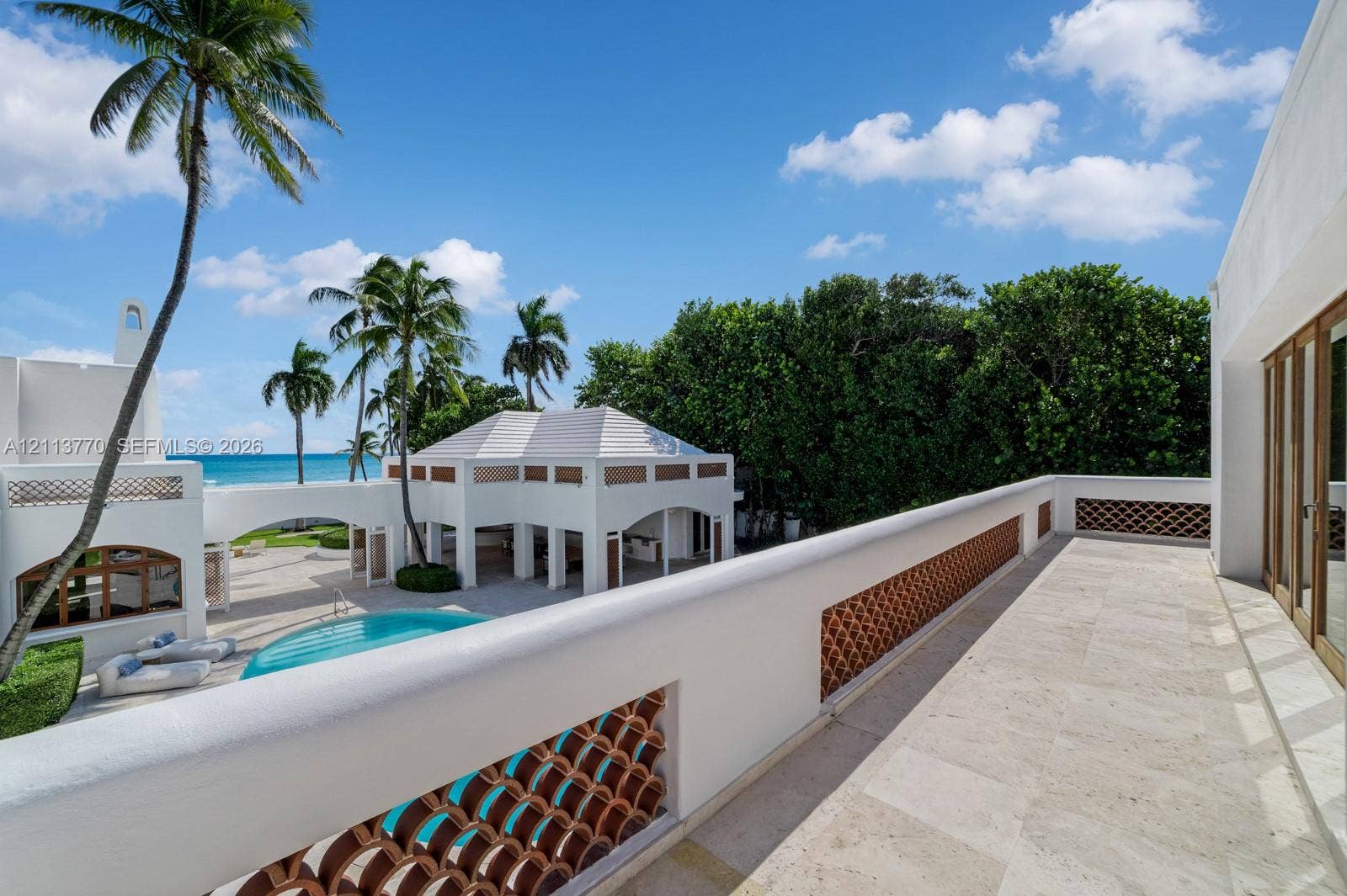 387 Ocean Boulevard, Golden Beach, Golden Beach, FL 33160 Second-story balcony featuring stone flooring and decorative terracotta balustrades, overlooking an outdoor pool area with a covered pavilion and tropical landscaping