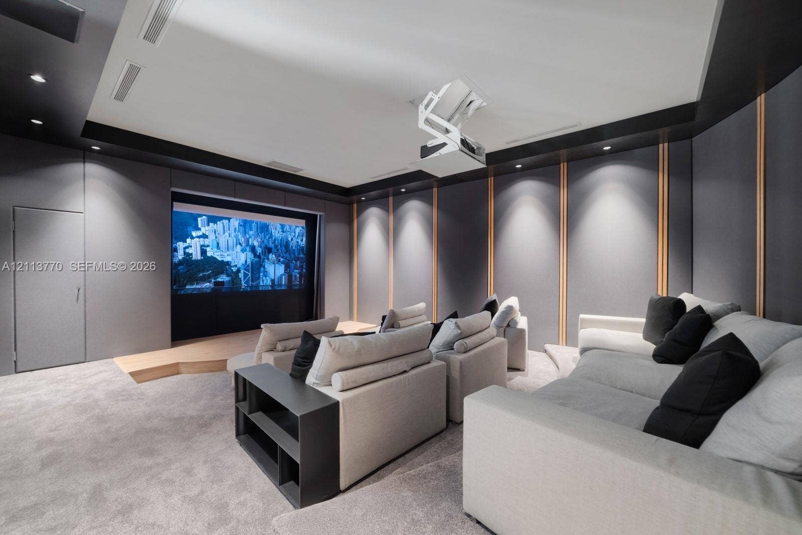 387 Ocean Boulevard, Golden Beach, Golden Beach, FL 33160 Media room featuring tiered flooring, custom acoustic wall paneling with integrated wood slats, recessed ceiling lighting, and a mounted overhead projector