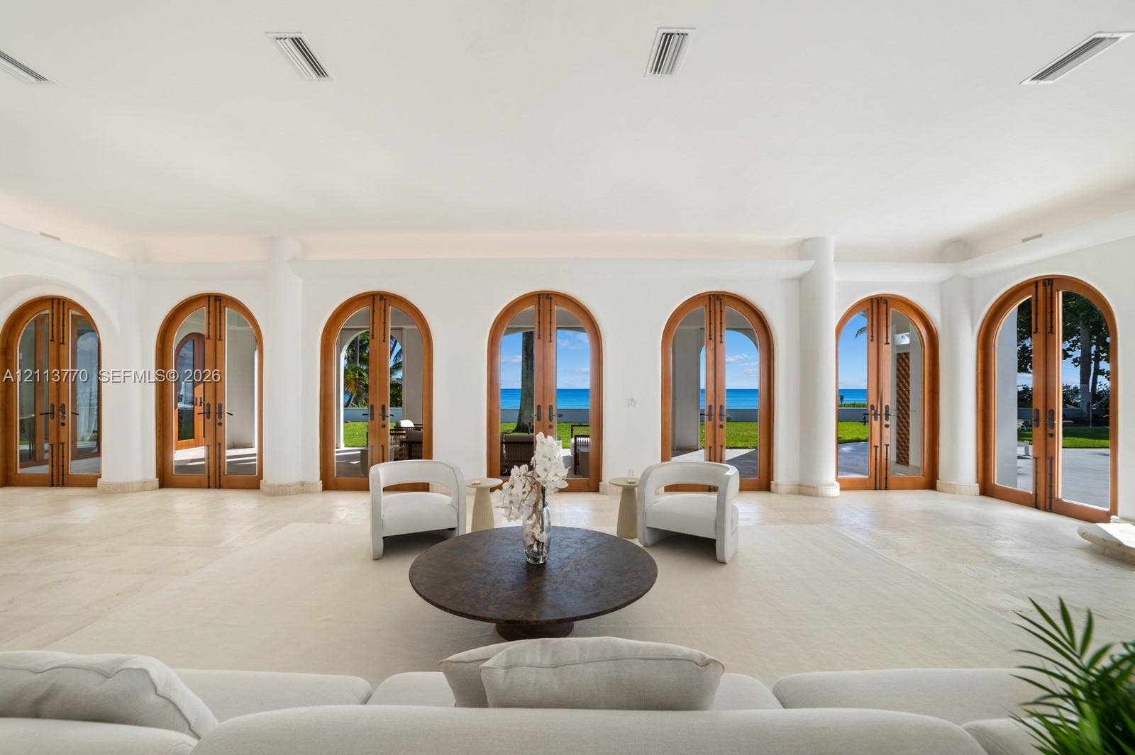 387 Ocean Boulevard, Golden Beach, Golden Beach, FL 33160 Living area featuring arched wood-framed glass double doors, large-format stone flooring, structural columns, and recessed ceiling lighting