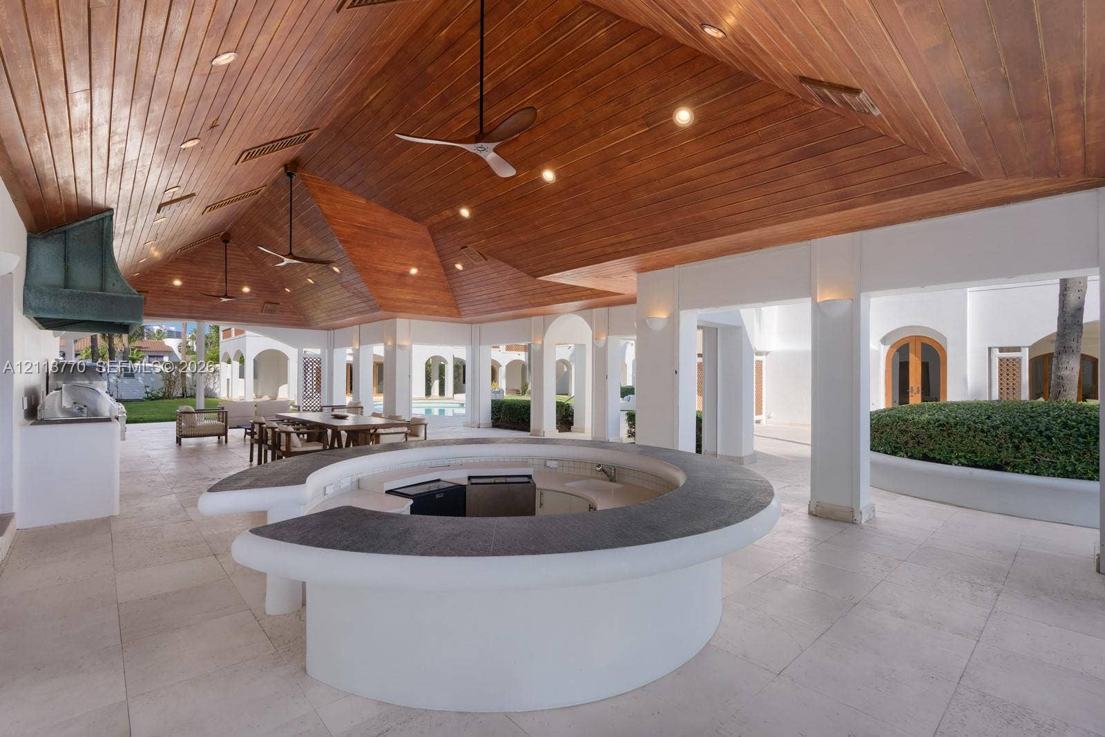 387 Ocean Boulevard, Golden Beach, Golden Beach, FL 33160 Covered outdoor patio featuring a vaulted tongue-and-groove wood ceiling, a circular concrete bar with a dark stone-finish countertop, stone flooring, and built-in recessed lighting