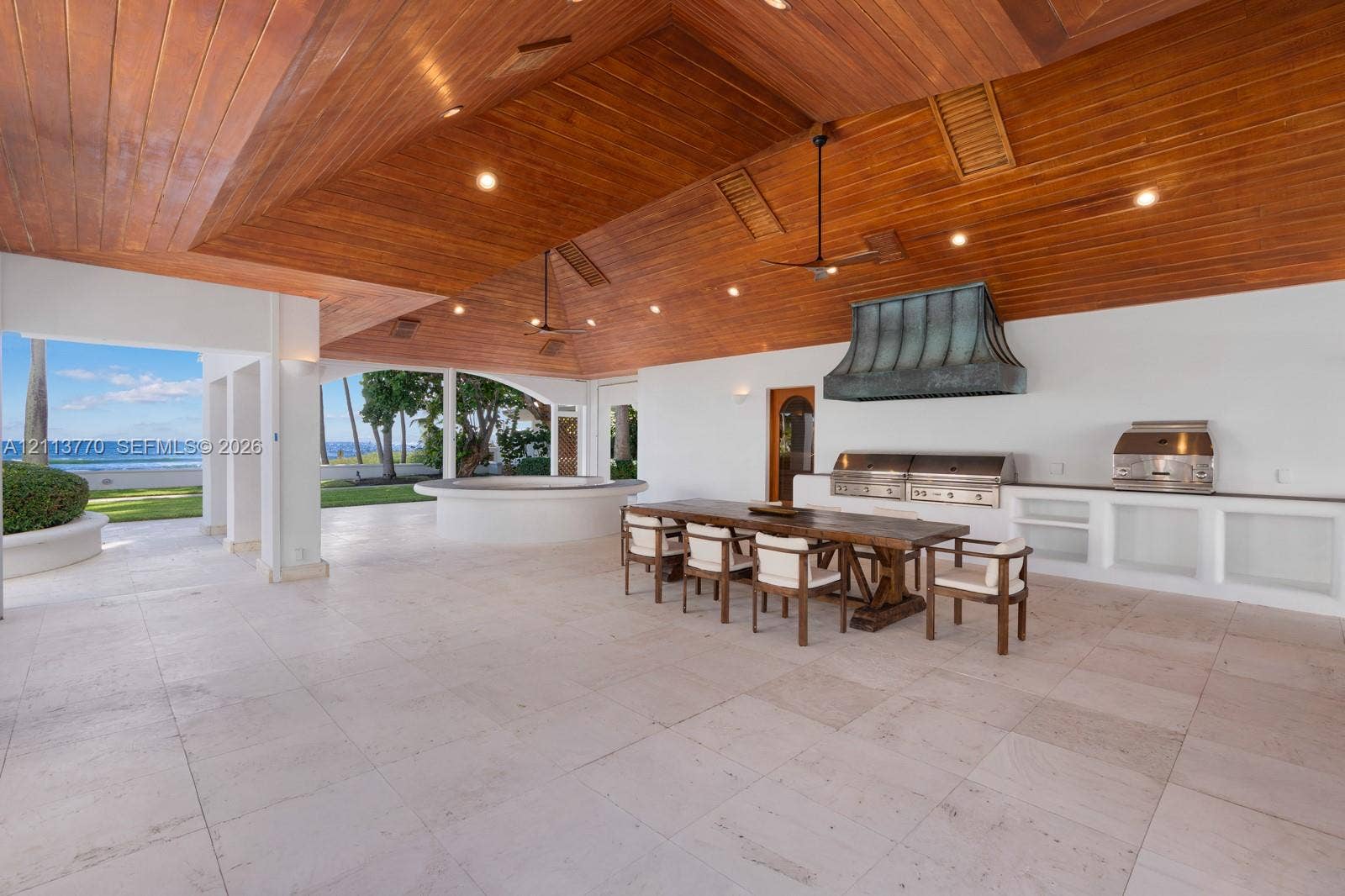 387 Ocean Boulevard, Golden Beach, Golden Beach, FL 33160 Covered outdoor kitchen featuring vaulted wood-paneled ceilings, stone flooring, built-in stainless steel appliances, and a custom metal range hood