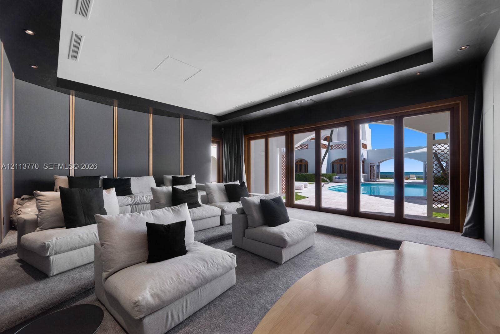 387 Ocean Boulevard, Golden Beach, Golden Beach, FL 33160 Media room featuring tiered flooring, decorative wall paneling with metallic accents, recessed ceiling lighting, and expansive multi-panel wood-framed glass doors