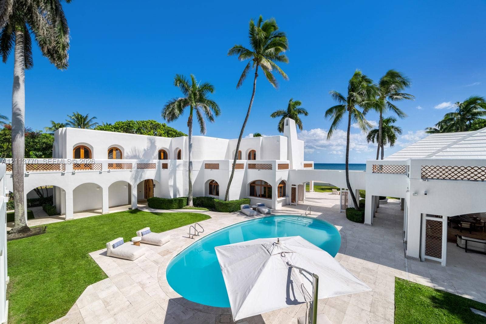 387 Ocean Boulevard, Golden Beach, Golden Beach, FL 33160 Mediterranean-style exterior featuring arched colonnades, white stucco finish, second-story decorative lattice railings, a private swimming pool with stone decking, and mature palm trees