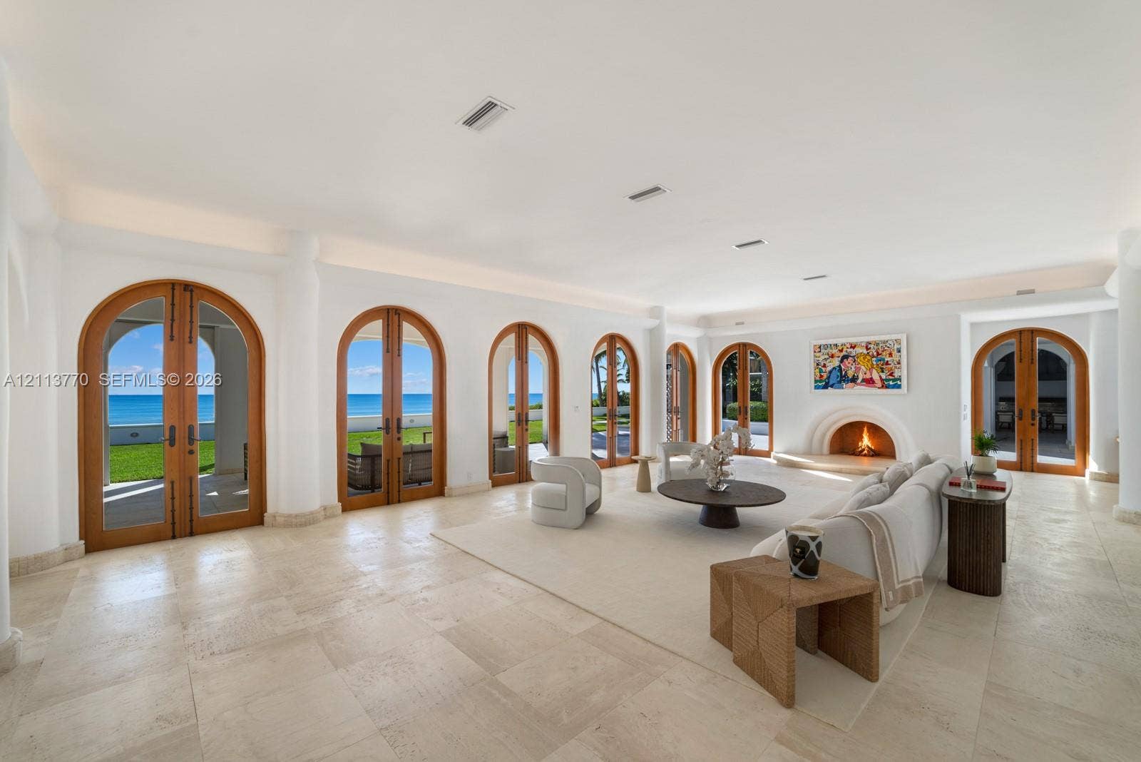 387 Ocean Boulevard, Golden Beach, Golden Beach, FL 33160 Living space featuring large-format stone flooring, multiple arched wood-frame glass doors, built-in recessed cove lighting, and an arched masonry fireplace