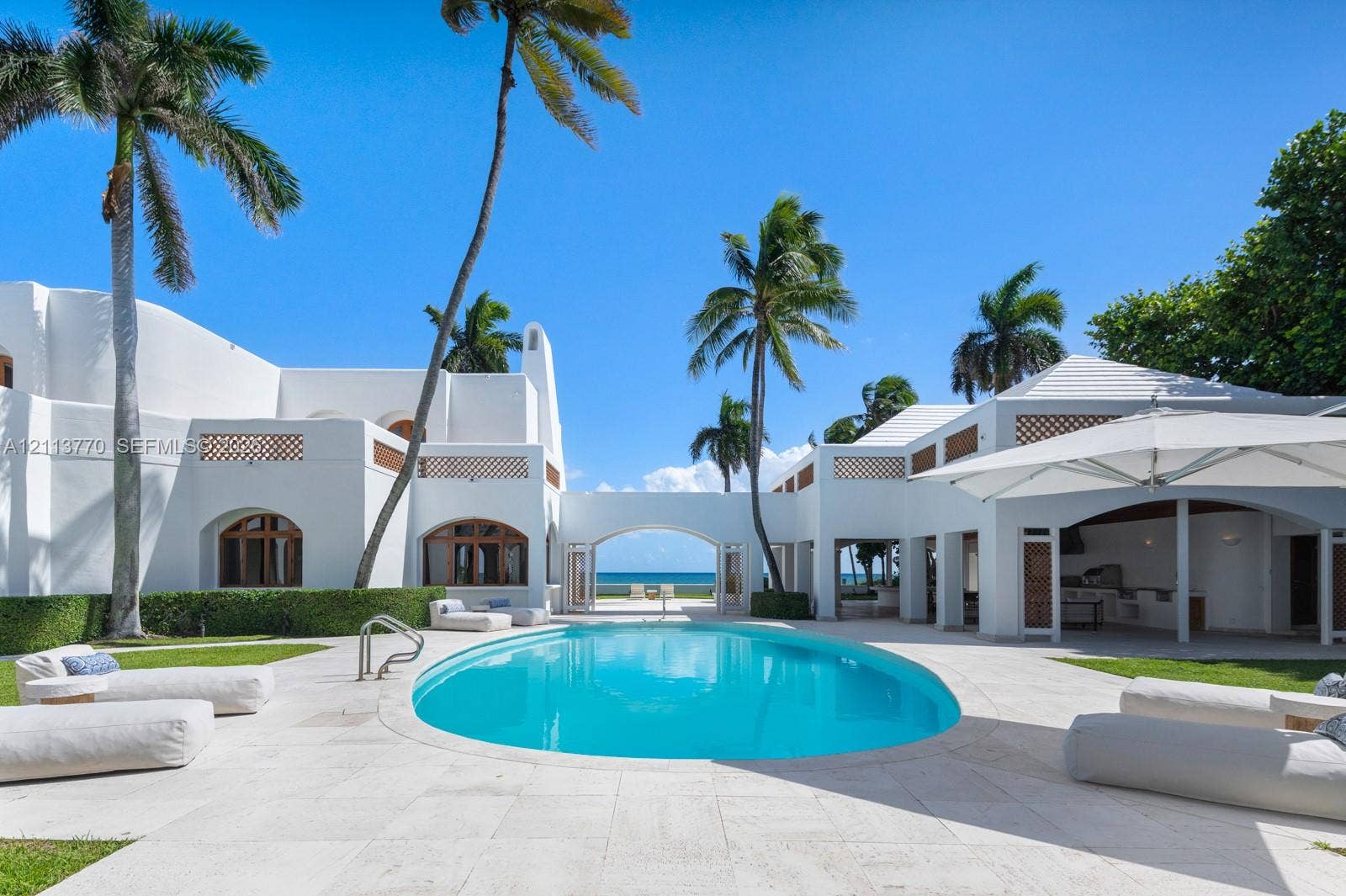 387 Ocean Boulevard, Golden Beach, Golden Beach, FL 33160 Exterior courtyard featuring an oval swimming pool, stone paved decking, stucco architecture with lattice accents, and an integrated outdoor kitchen