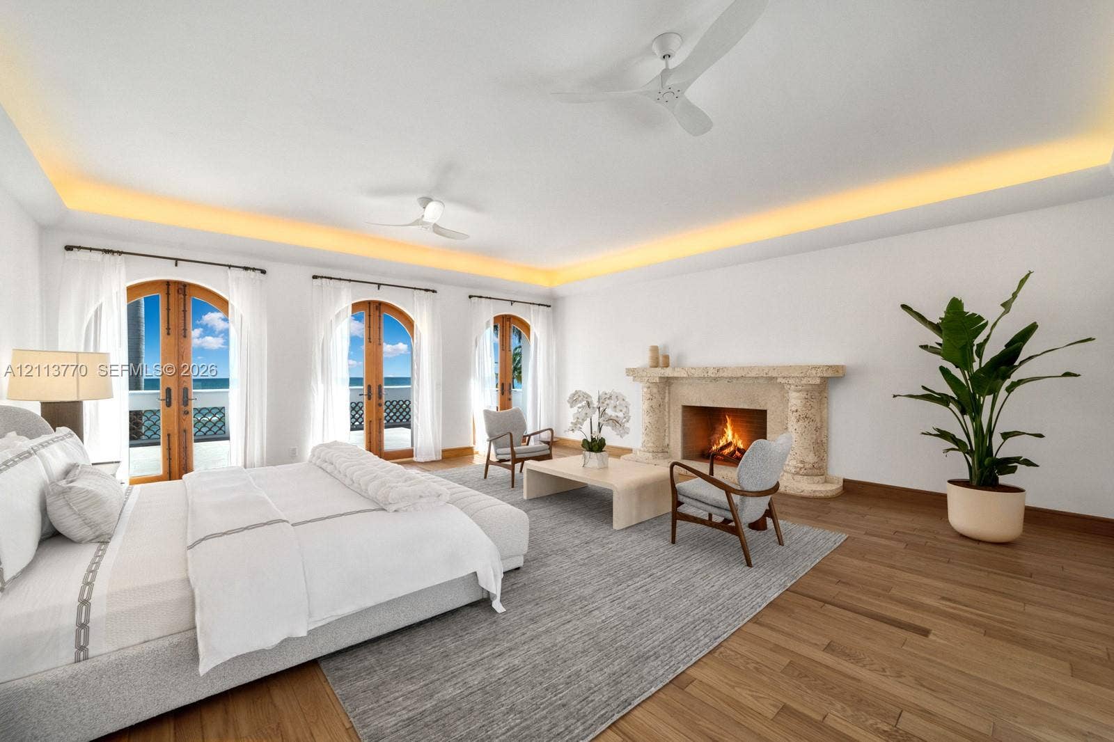 387 Ocean Boulevard, Golden Beach, Golden Beach, FL 33160 Spacious room featuring wood-finish flooring, recessed tray ceiling lighting, three sets of arched wooden-framed glass doors, and a limestone-surround fireplace with decorative columns