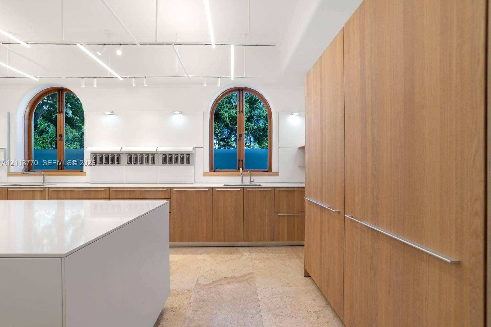 387 Ocean Boulevard, Golden Beach, Golden Beach, FL 33160 Kitchen featuring light-finish wood cabinetry, a solid-surface center island, arched windows with wood frames, stone tile flooring, and integrated linear overhead lighting