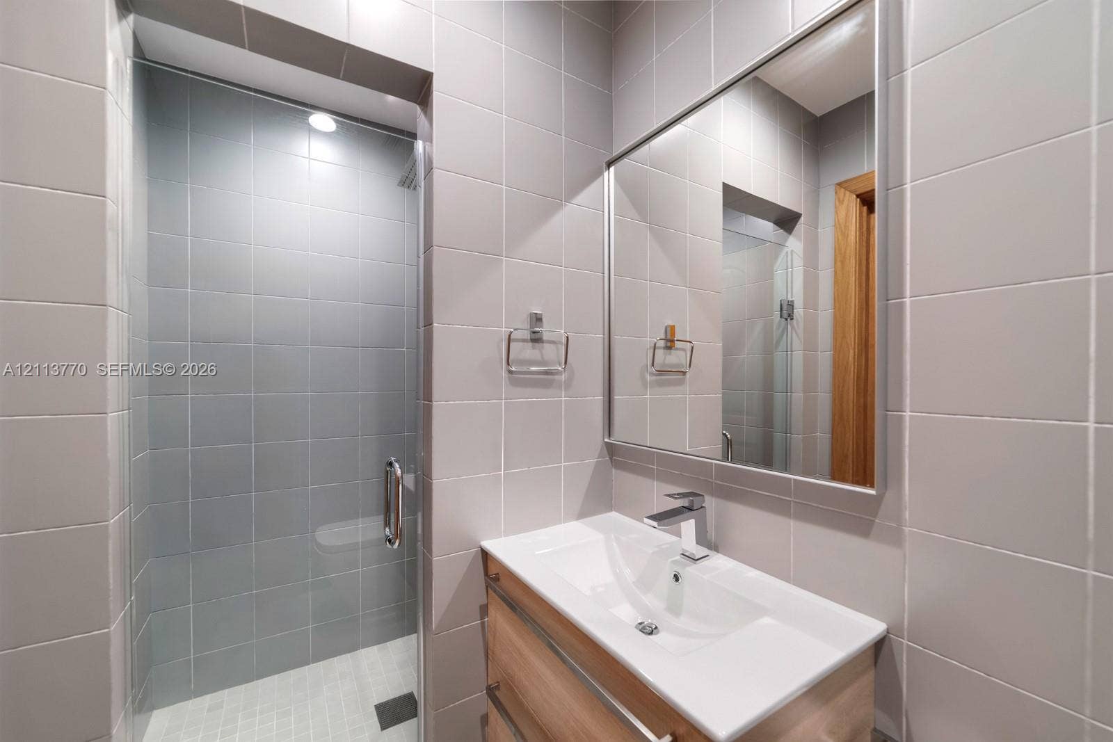 387 Ocean Boulevard, Golden Beach, Golden Beach, FL 33160 Bathroom featuring a light wood-finish floating vanity with a white integrated sink, chrome single-lever faucet, wall-to-wall square ceramic tiling, and a glass-enclosed shower