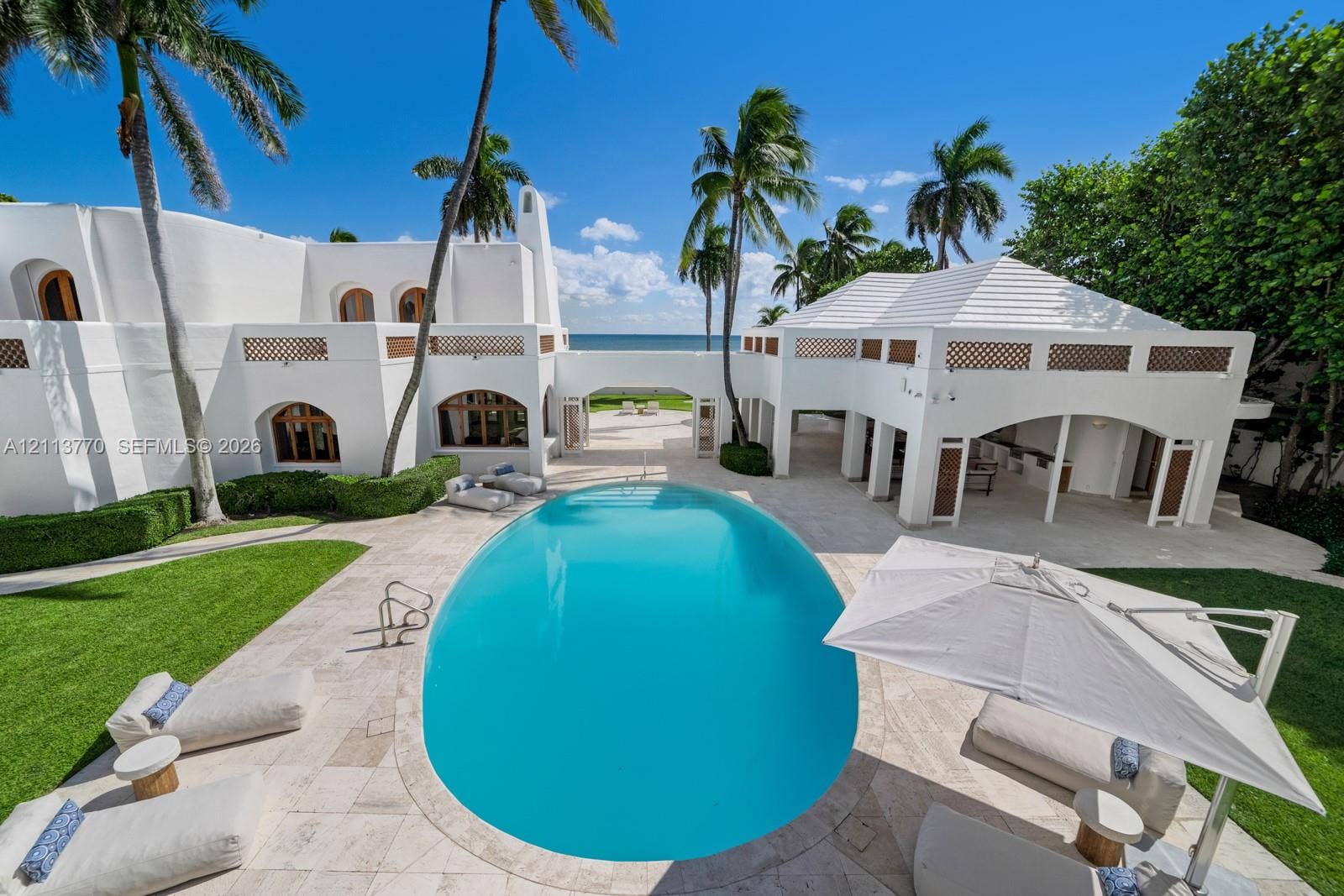 387 Ocean Boulevard, Golden Beach, Golden Beach, FL 33160 Stucco exterior featuring arched architectural detailing, a central swimming pool with stone-tiled decking, a covered outdoor loggia, and integrated privacy hedging