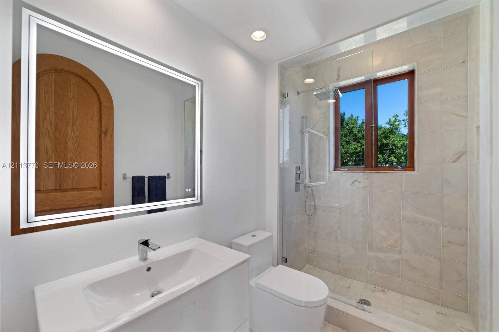 387 Ocean Boulevard, Golden Beach, Golden Beach, FL 33160 Full bathroom featuring a glass-enclosed shower with tiled surround, light-toned stone-finish flooring, a wall-mounted LED mirror, and a white vanity with an integrated basin