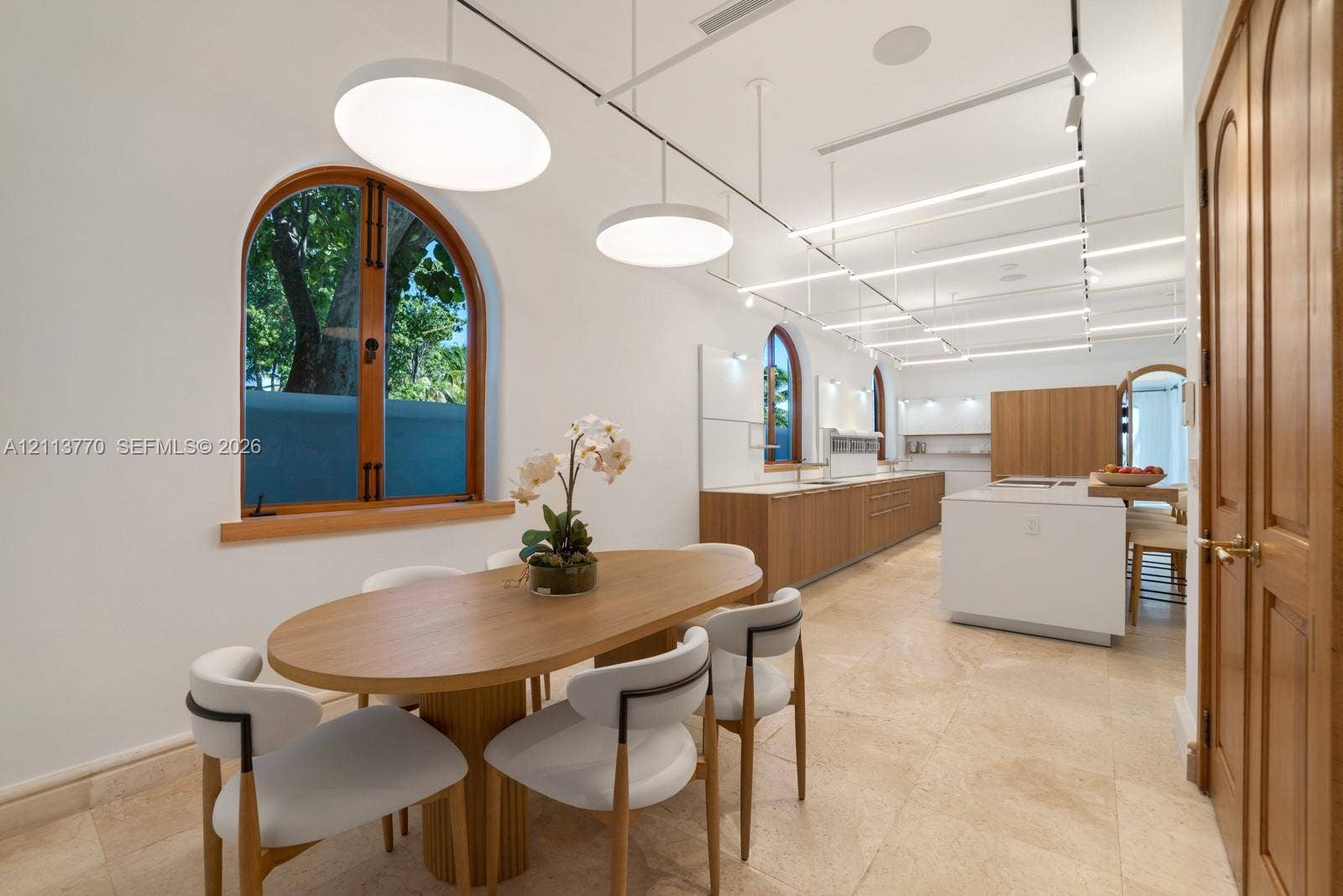 387 Ocean Boulevard, Golden Beach, Golden Beach, FL 33160 Open-concept space featuring arched wood-framed windows, stone flooring, integrated linear track lighting, and a kitchen island with built-in cabinetry