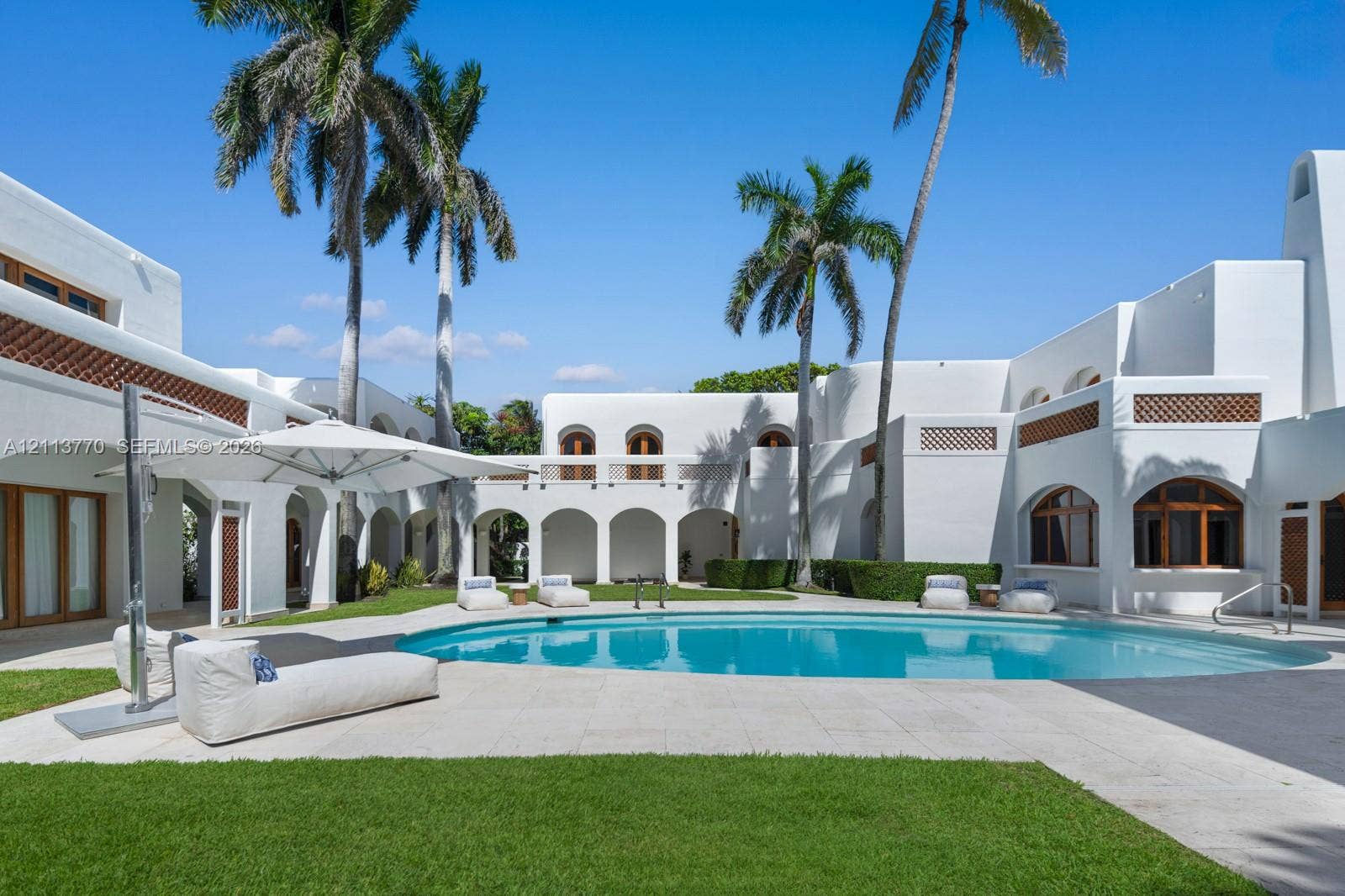 387 Ocean Boulevard, Golden Beach, Golden Beach, FL 33160 Courtyard featuring a curved swimming pool, stone patio, arched loggia, stucco exterior, and decorative lattice detailing