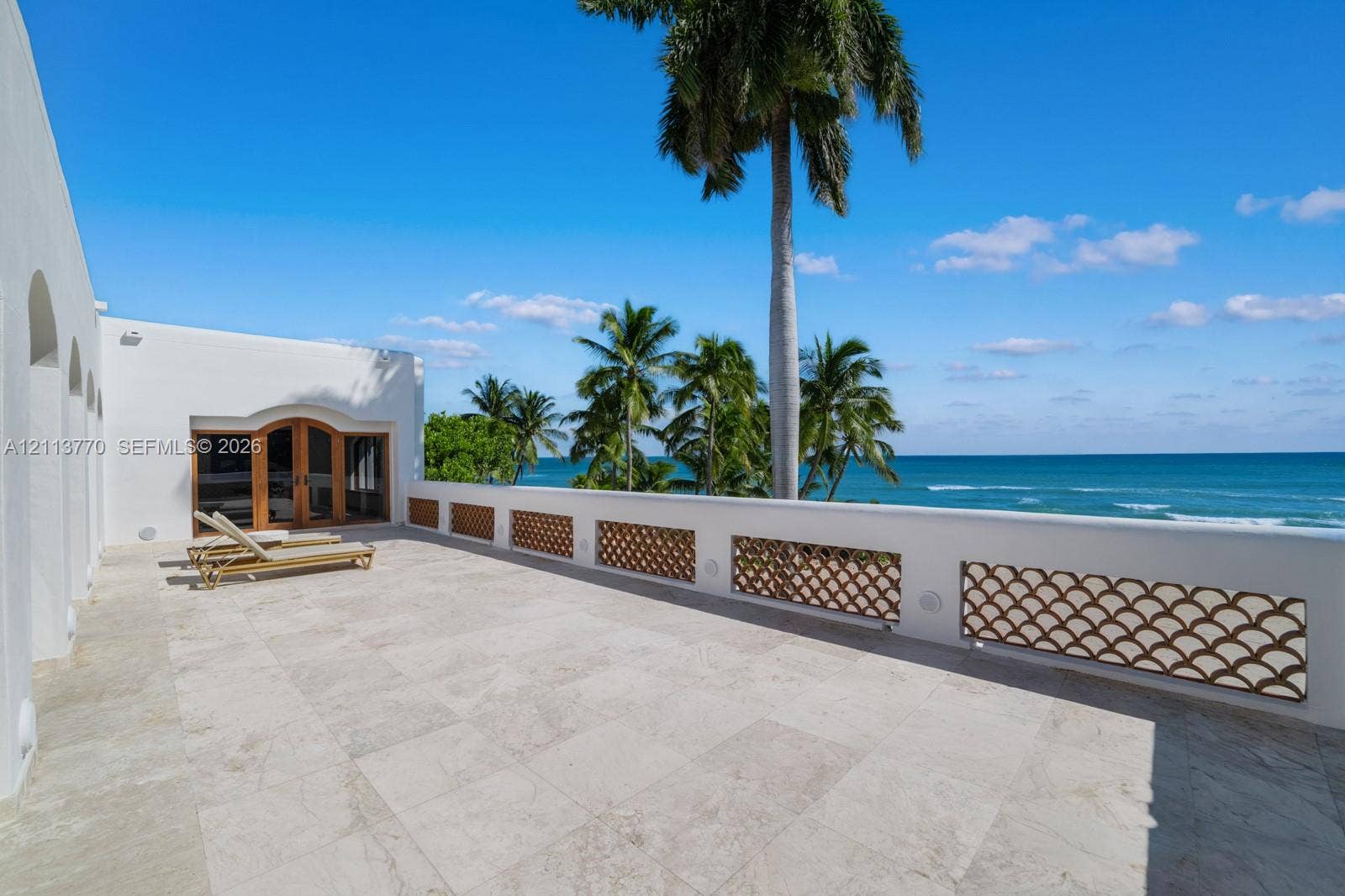 387 Ocean Boulevard, Golden Beach, Golden Beach, FL 33160 Expansive stone terrace featuring decorative metal balustrades, arched wood-framed glass double doors, and ocean frontage