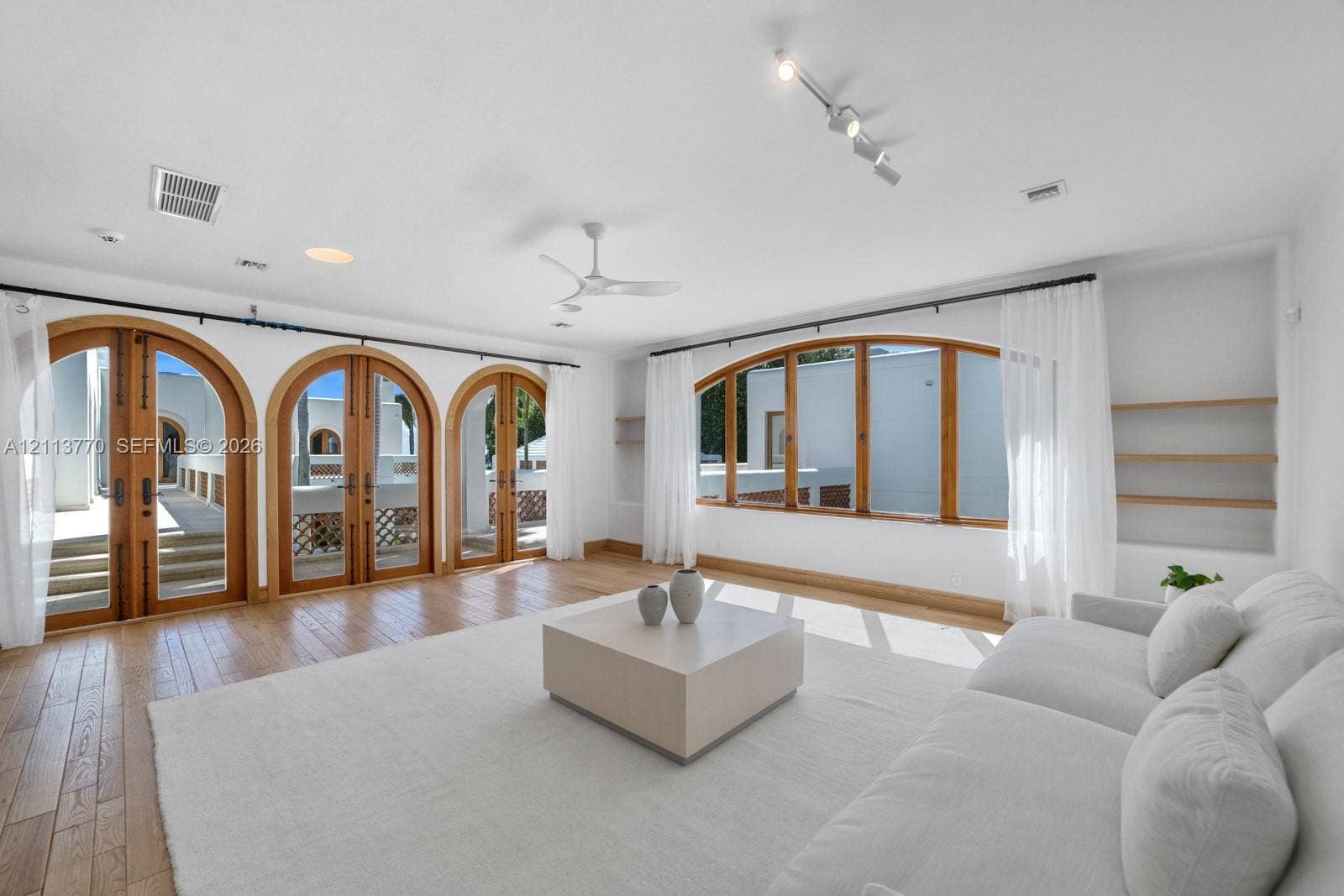 387 Ocean Boulevard, Golden Beach, Golden Beach, FL 33160 Living space featuring arched wood-framed doors, wood-finish flooring, built-in wall shelving, a ceiling fan, and adjustable track lighting