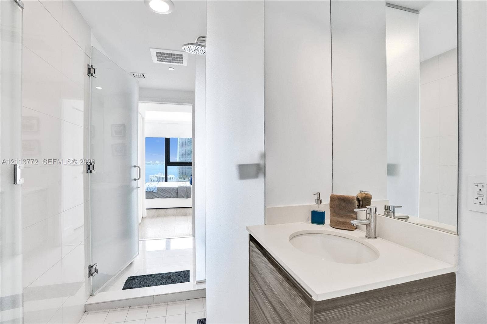 Bathroom featuring a wood-finish vanity with a light-toned countertop, integrated sink, chrome faucet, glass-enclosed shower, and full-height wall mirror