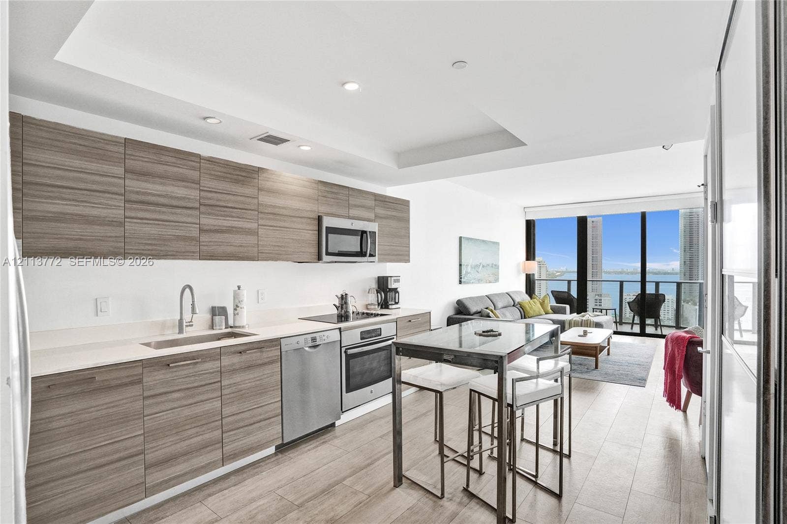 Kitchen featuring horizontal wood-grain cabinetry, stainless steel appliances, recessed ceiling lighting, and wood-finish flooring with floor-to-ceiling windows