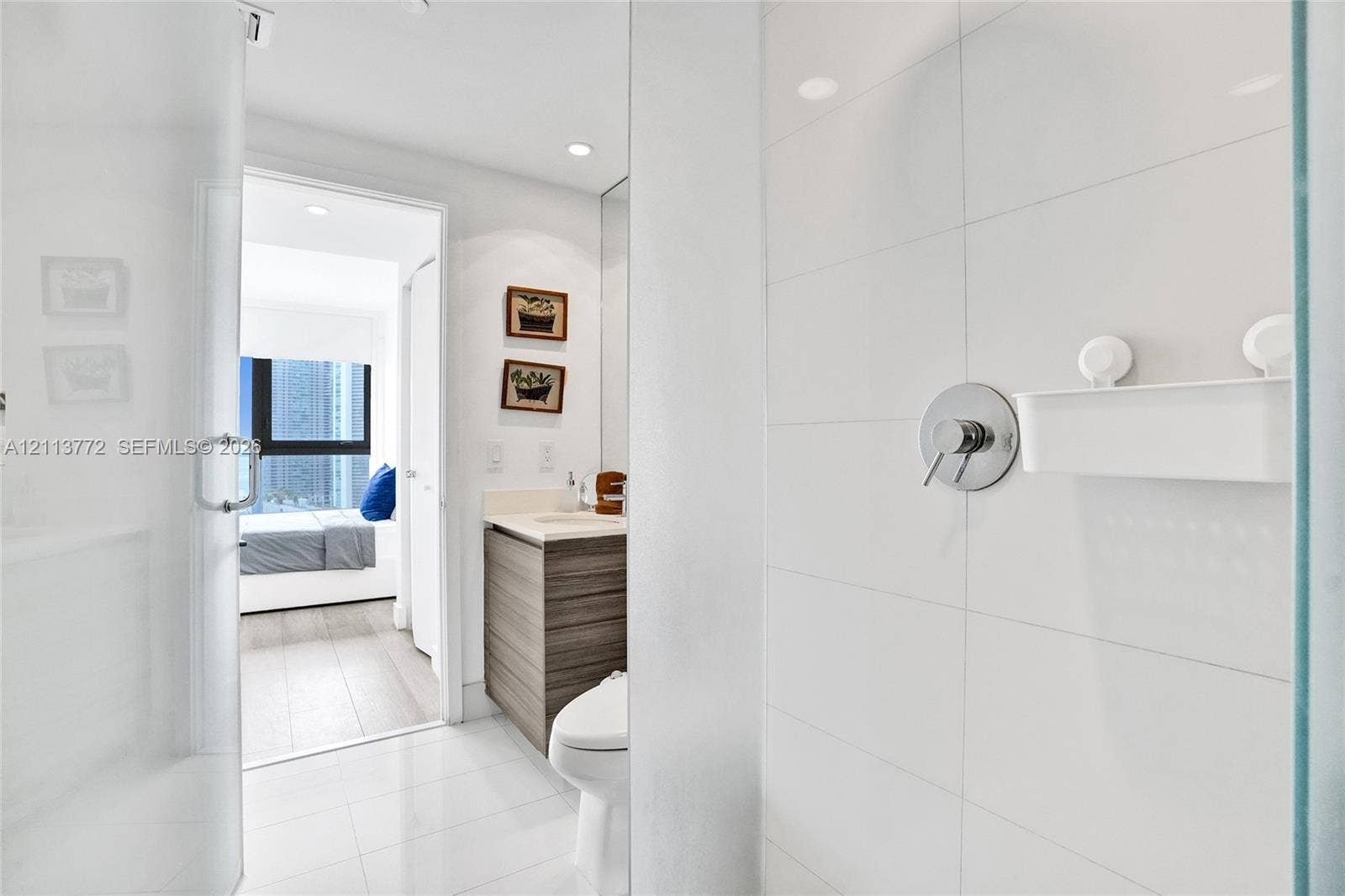 Full-height white tile shower enclosure featuring polished chrome fixtures, glass door, wood-finish cabinetry, and solid surface countertop