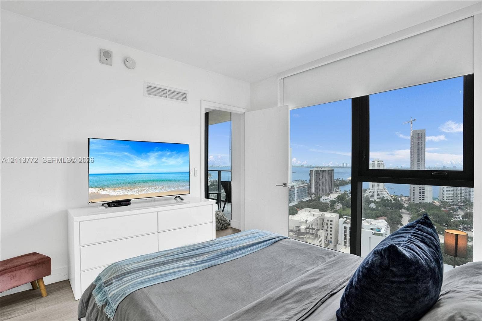Floor-to-ceiling windows with expansive urban and water scenery, wood-finish flooring, and access to a private balcony