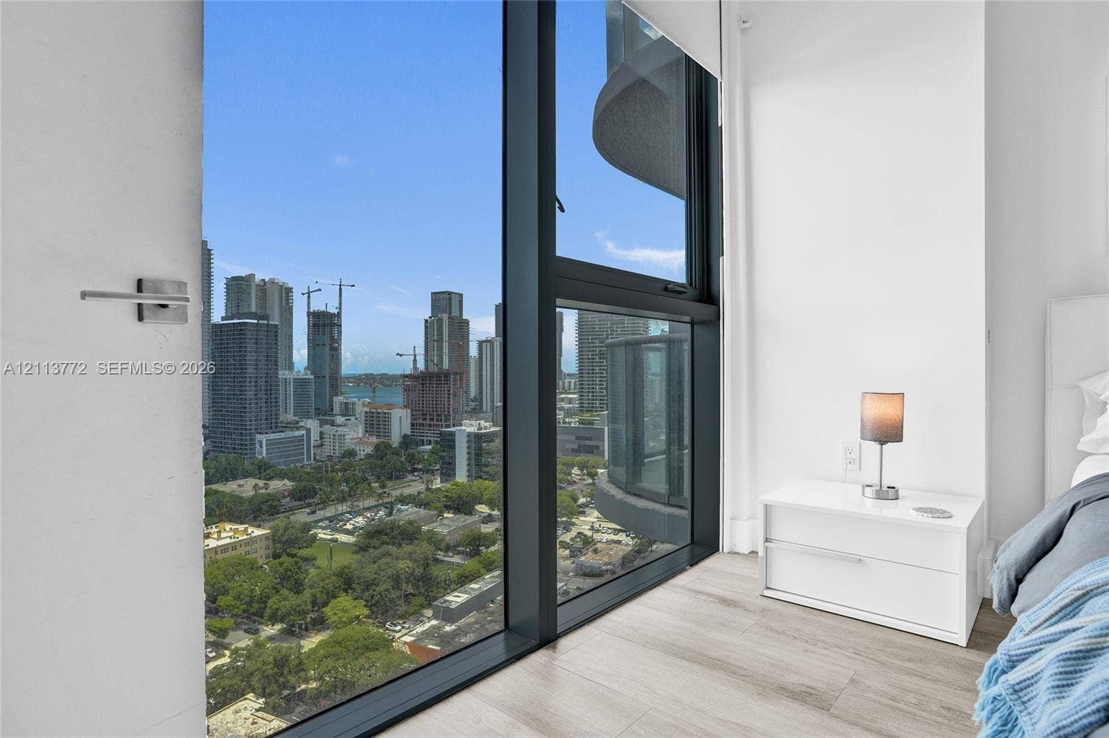 Floor-to-ceiling windows featuring dark metal framing, wood-finish flooring, and expansive urban scenery