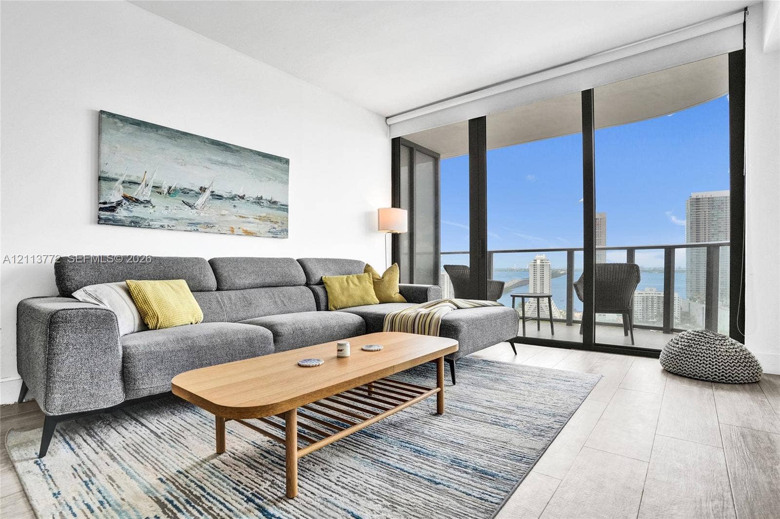 Floor-to-ceiling windows, wood-finish flooring, and a private balcony with metal railing