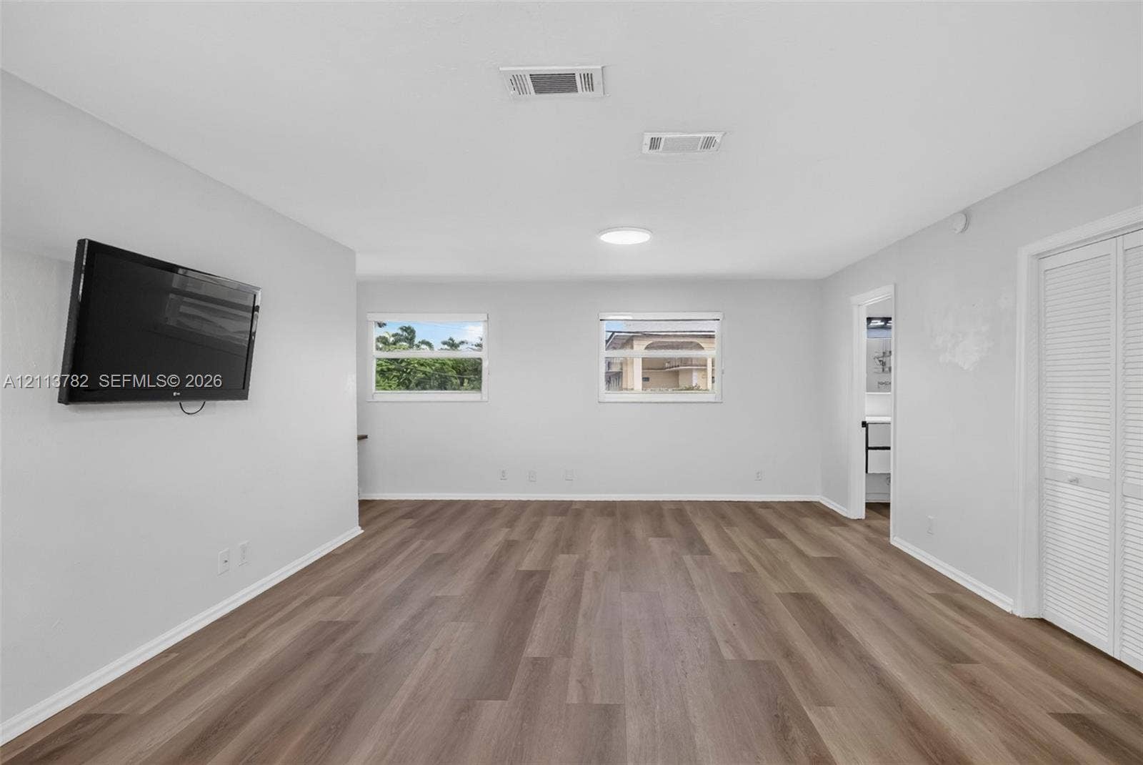 4720 Bayview Drive, Fort Lauderdale, FL 33308 Neutral interior featuring wood-finish flooring, two dual-pane windows, and white bifold closet doors