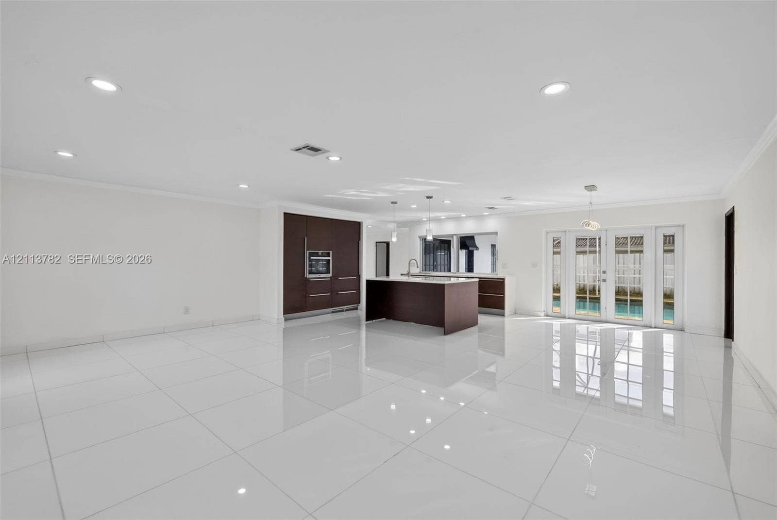 4720 Bayview Drive, Fort Lauderdale, FL 33308 Open-concept kitchen featuring dark wood-finish cabinetry, a central island, recessed lighting, and white tile flooring throughout, accented by French doors