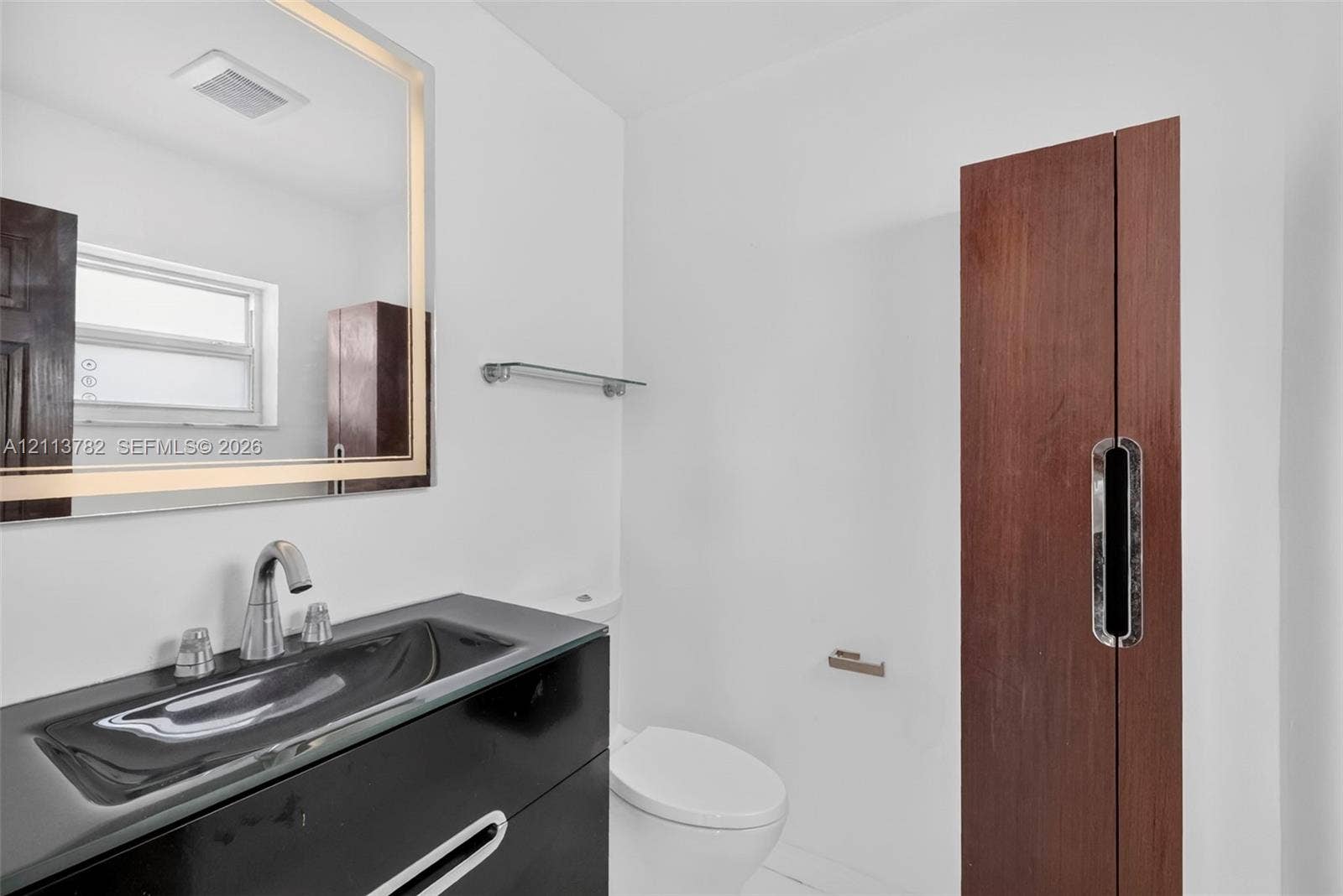 4720 Bayview Drive, Fort Lauderdale, FL 33308 Modern vanity with an integrated sink, backlit rectangular mirror, sleek wood-finish cabinetry, and contemporary polished-chrome fixtures