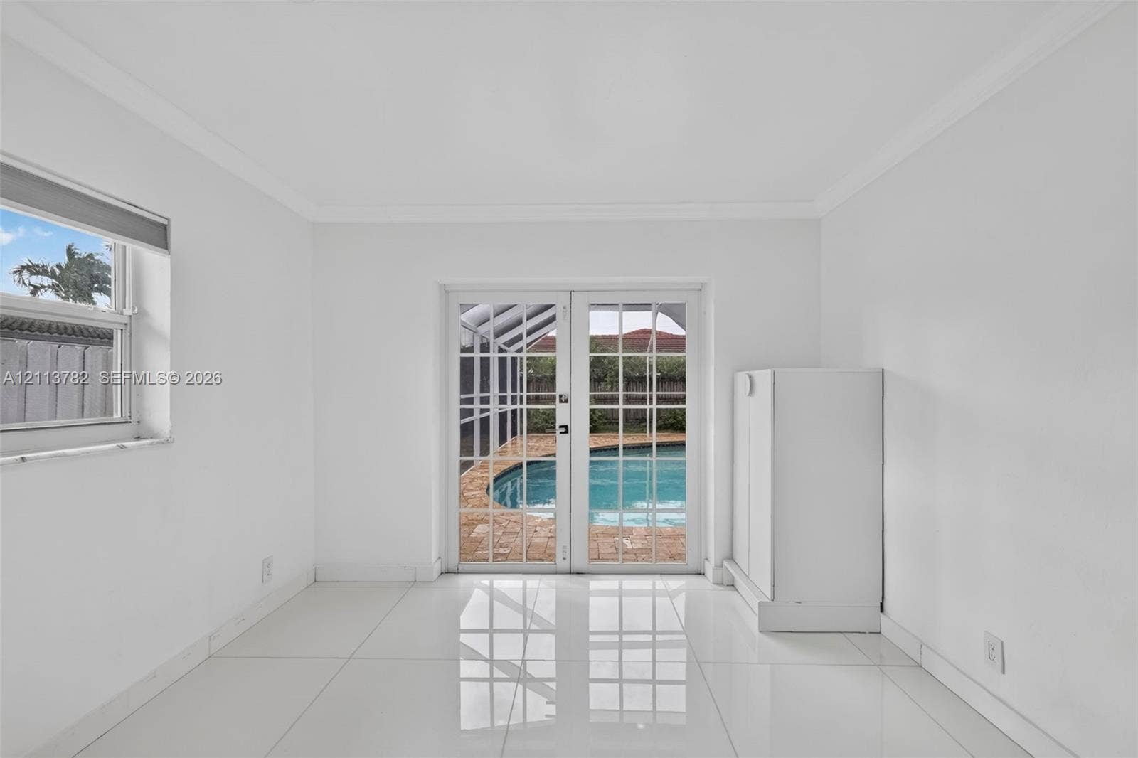4720 Bayview Drive, Fort Lauderdale, FL 33308 Interior space featuring white tile flooring, crown molding, double French doors, and built-in white cabinetry, with a perspective toward a screened pool enclosure