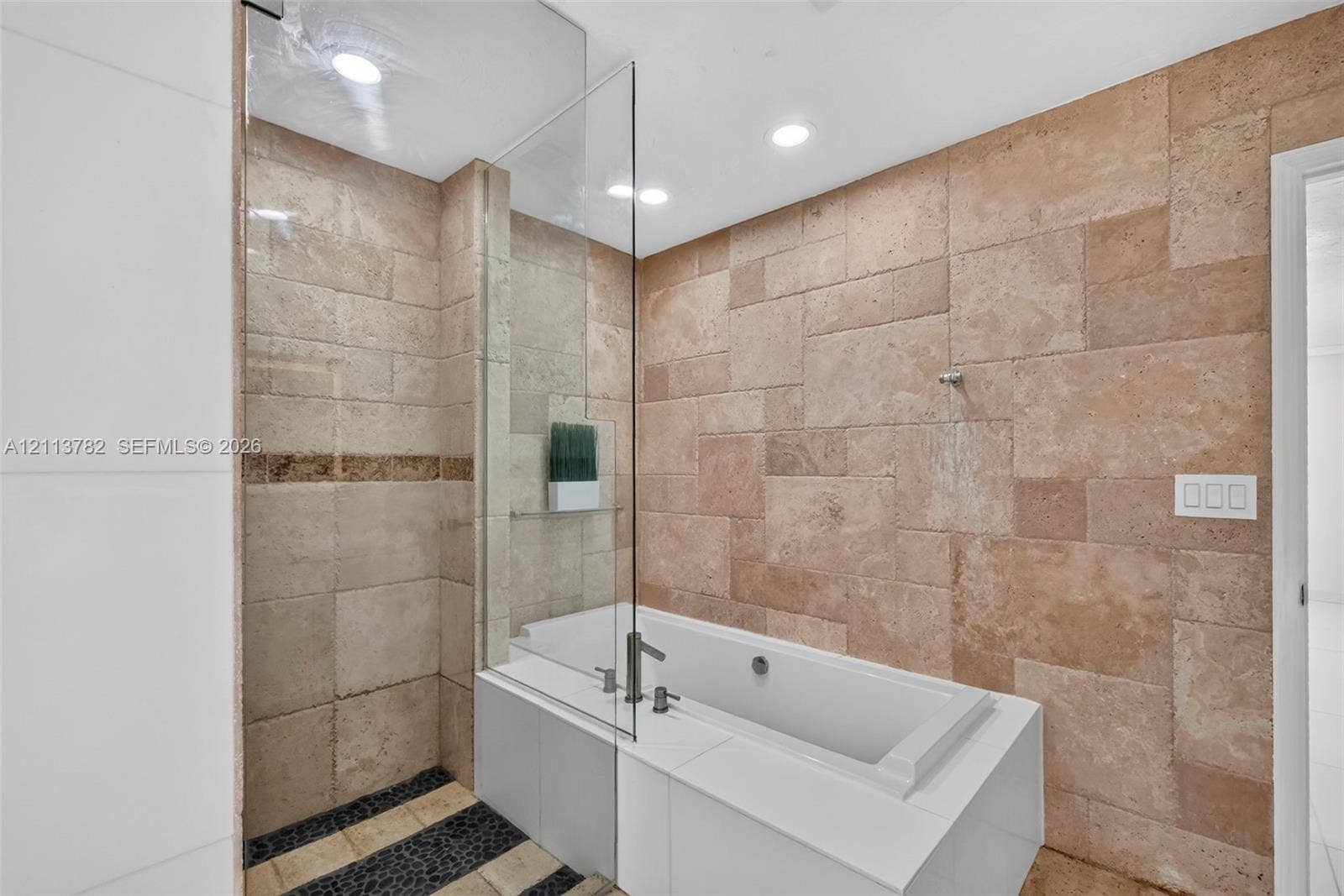 4720 Bayview Drive, Fort Lauderdale, FL 33308 Large-format natural stone wall tiling, integrated soaking tub with a white surround, glass shower partition, recessed ceiling lighting, and pebble-style floor inlay