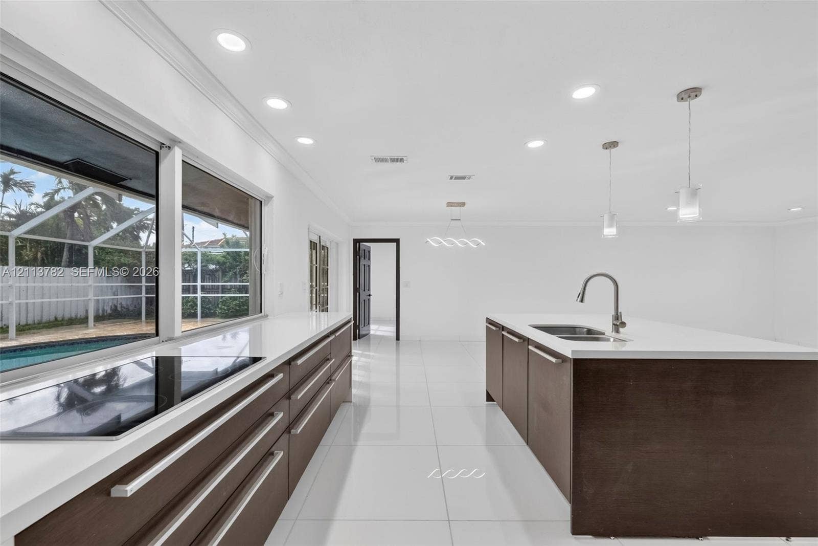 4720 Bayview Drive, Fort Lauderdale, FL 33308 Kitchen featuring dark wood-finish cabinetry, solid-surface countertops, a center island with an undermount sink, porcelain tile flooring, and recessed lighting
