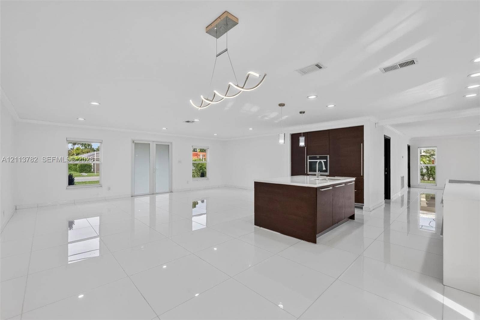 4720 Bayview Drive, Fort Lauderdale, FL 33308 Open-concept interior featuring large-format tile flooring, a center island with a stone countertop, dark wood-finish cabinetry, recessed lighting, and a modern sculptural chandelier