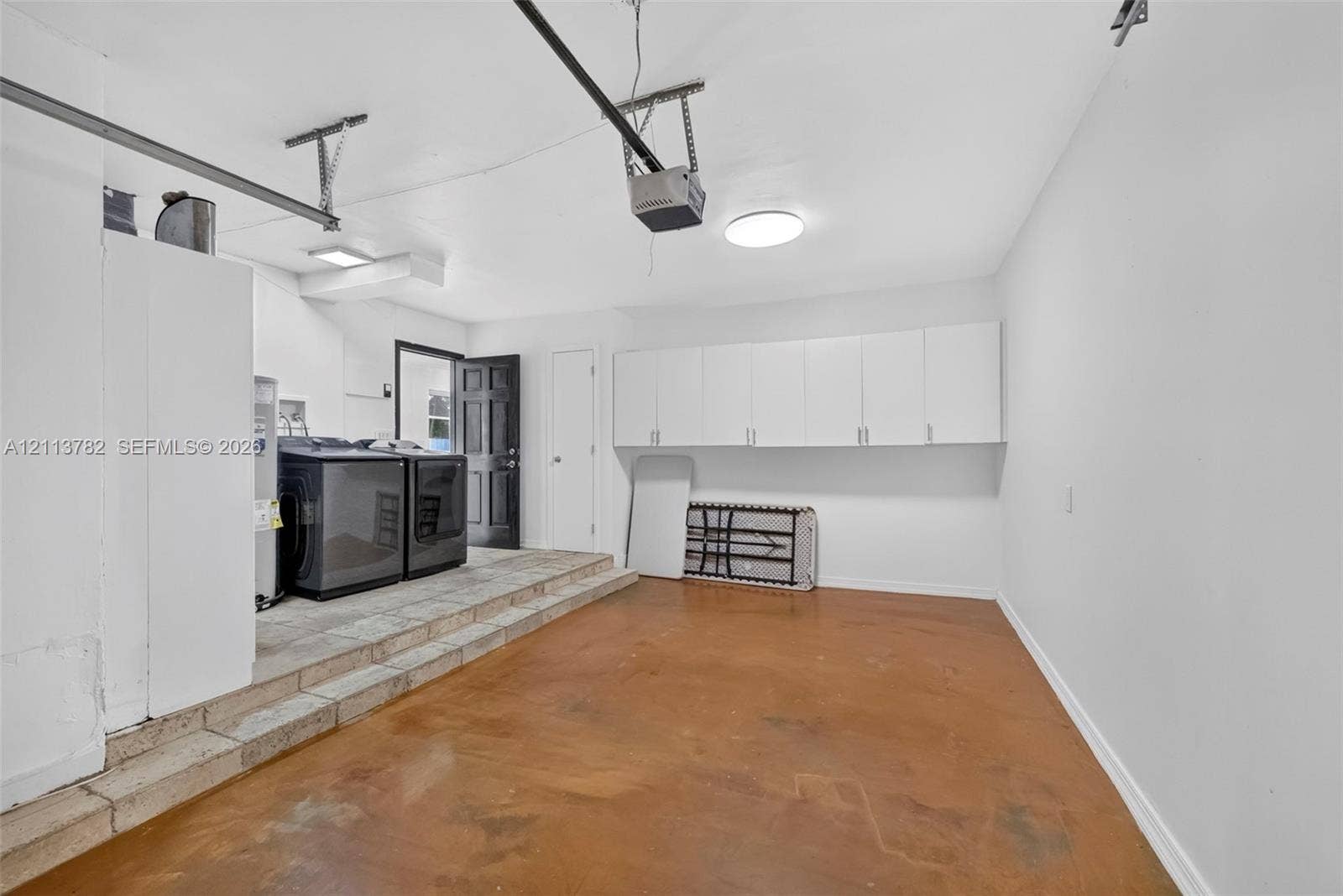 4720 Bayview Drive, Fort Lauderdale, FL 33308 Garage featuring stained concrete flooring, white wall-mounted storage cabinetry, raised utility platform, and exterior access door