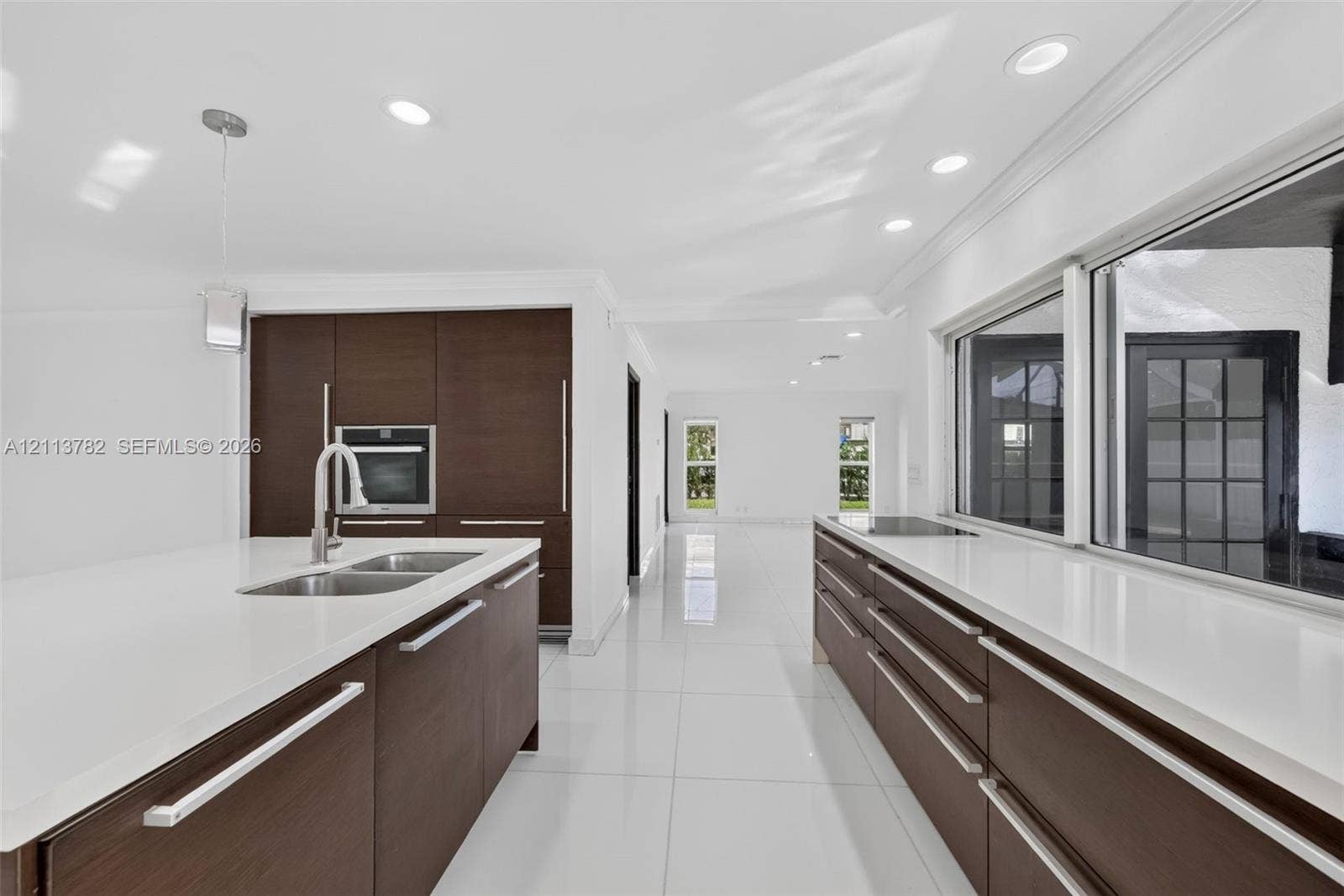 4720 Bayview Drive, Fort Lauderdale, FL 33308 Kitchen featuring dark wood-finish cabinetry, solid-surface countertops, integrated wall oven, stainless steel dual-basin sink with pull-down faucet, and polished tile flooring