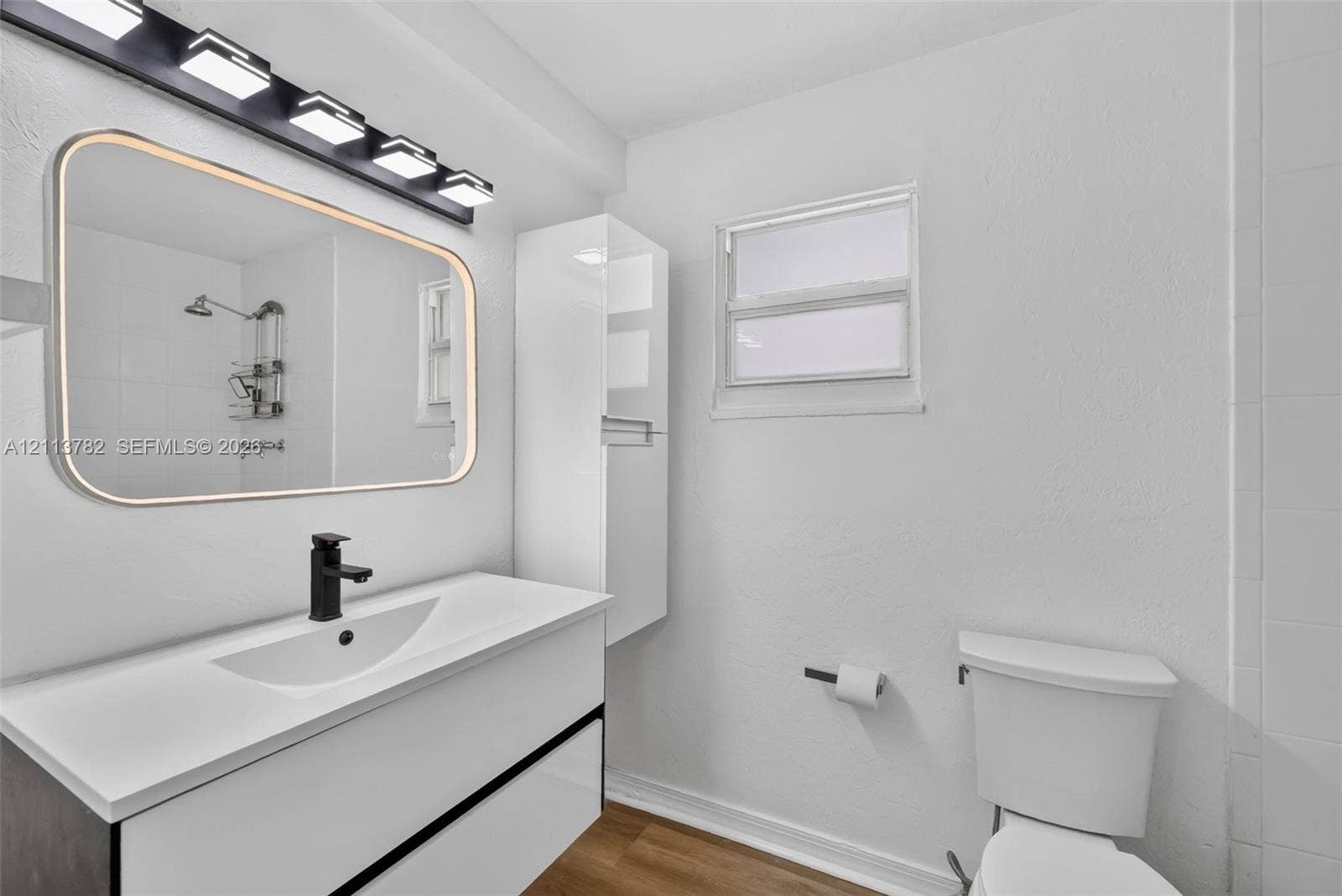 4720 Bayview Drive, Fort Lauderdale, FL 33308 Bathroom featuring a floating vanity with a integrated basin, matte black faucet, wall-mounted storage cabinet, and large rectangular mirror with perimeter lighting