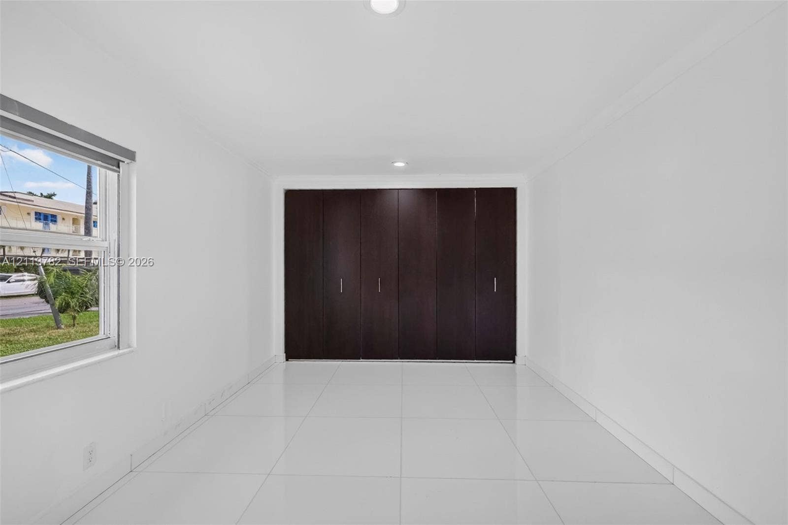4720 Bayview Drive, Fort Lauderdale, FL 33308 Interior space featuring large-format white tile flooring, recessed ceiling lighting, and floor-to-ceiling built-in cabinetry with dark wood-finish paneling