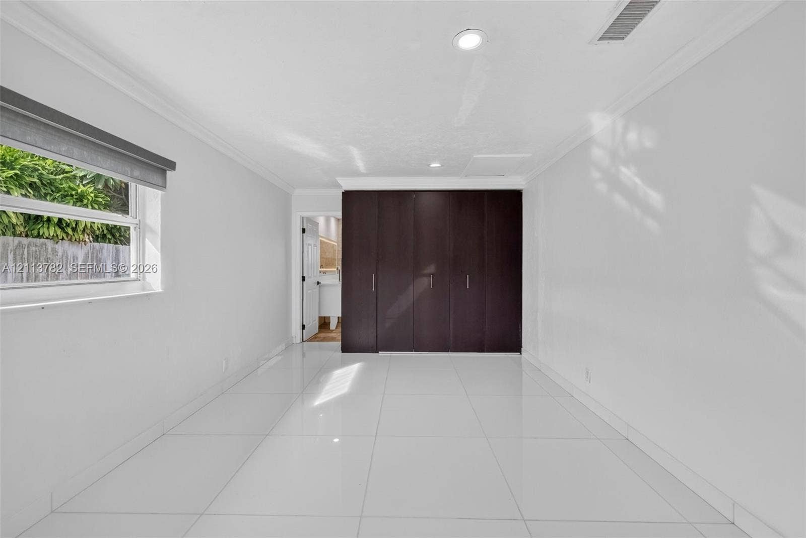 4720 Bayview Drive, Fort Lauderdale, FL 33308 Neutral-toned interior featuring large-format white tile flooring, crown molding, recessed lighting, and floor-to-ceiling built-in cabinetry with dark wood-finish doors