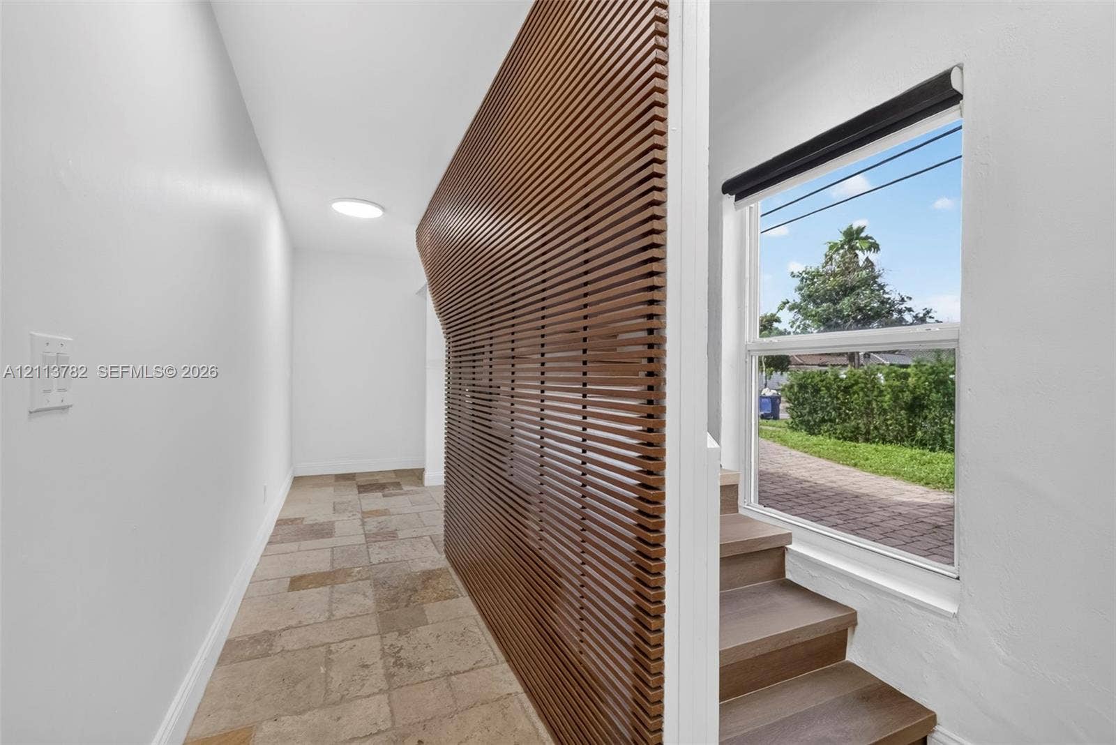 4720 Bayview Drive, Fort Lauderdale, FL 33308 Interior featuring a curved slat-wood wall partition, large-format stone tile flooring, and stairs with wood-finish treads beneath a single-hung window