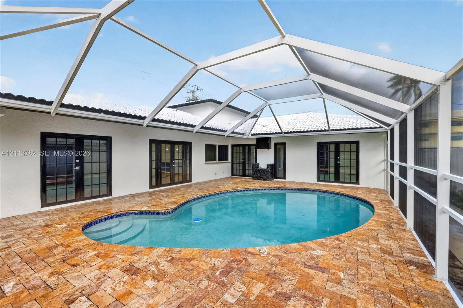 4720 Bayview Drive, Fort Lauderdale, FL 33308 Screened-in patio featuring a custom-shaped pool, natural stone paver deck, multiple glass-paned French doors, and a vaulted enclosure frame