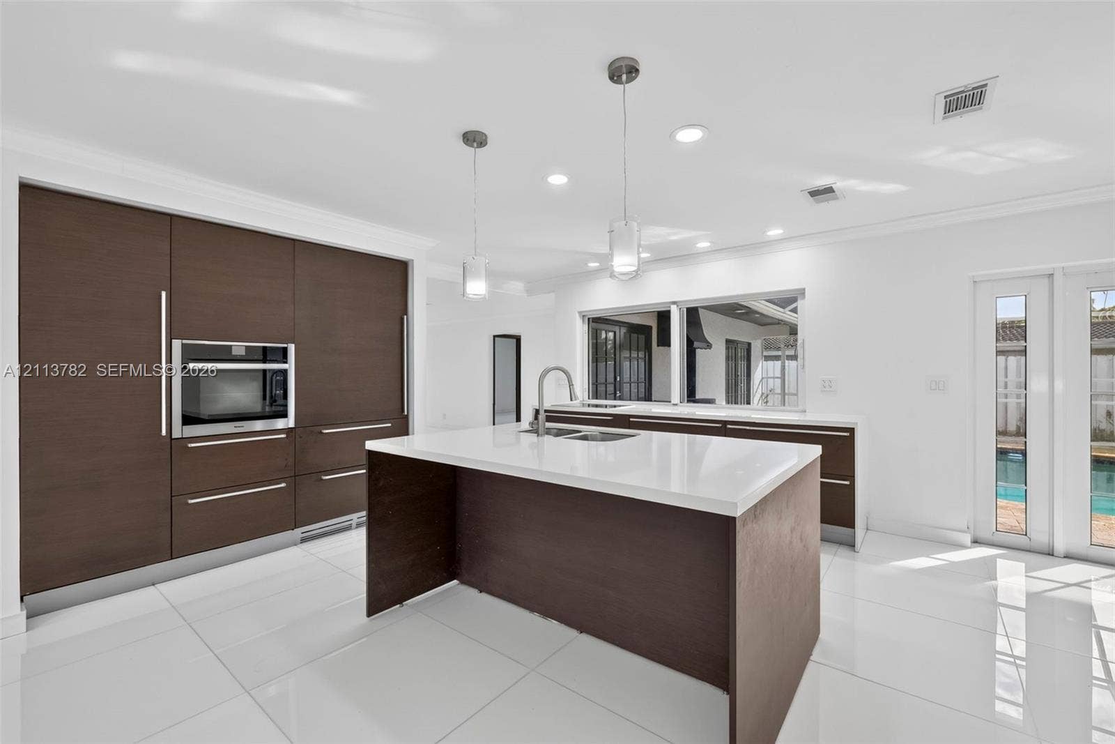 4720 Bayview Drive, Fort Lauderdale, FL 33308 Kitchen featuring dark wood-finish cabinetry, solid-surface countertops, a center island with a built-in sink, stainless steel wall oven, and polished tile flooring