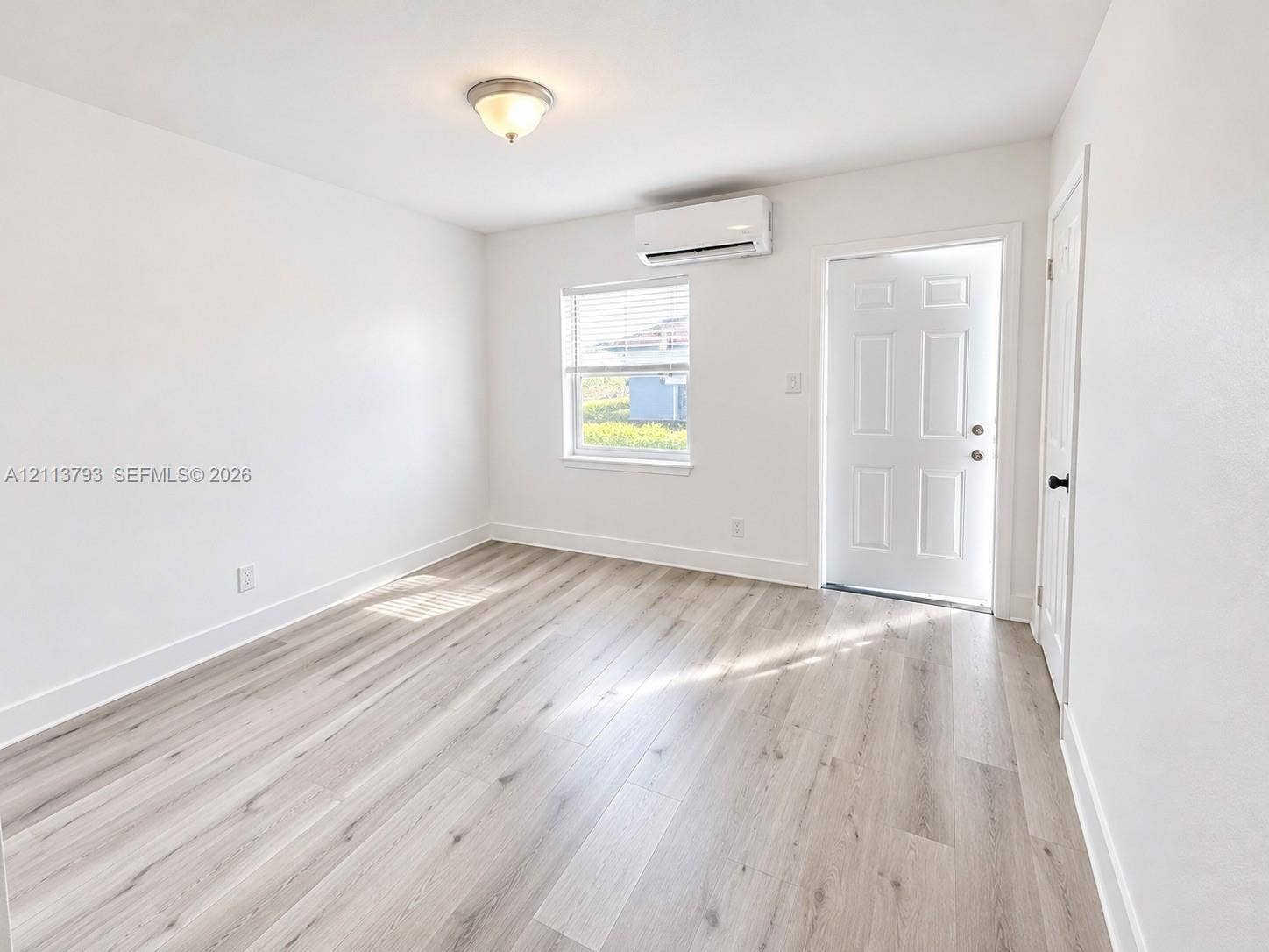 2638 Johnson Street, #53, Hollywood, Hollywood, FL 33020 Interior space featuring wood-finish flooring, a wall-mounted ductless mini-split air conditioning unit, a six-panel exterior entry door, and a single-hung window with blinds