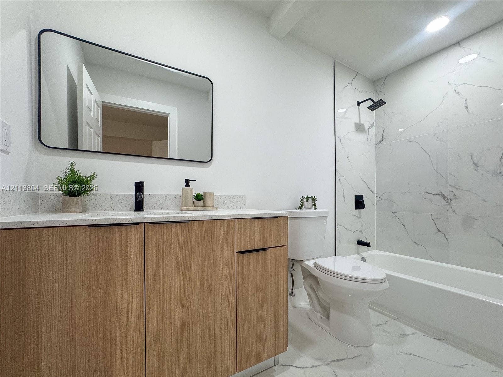 2300 NW 31st Avenue, Fort Lauderdale, FL 33311 Wood-finish cabinetry with a light-tone countertop, rectangular mirror with matte black framing, and tub-shower combination featuring large-format wall tiling and matte black hardware