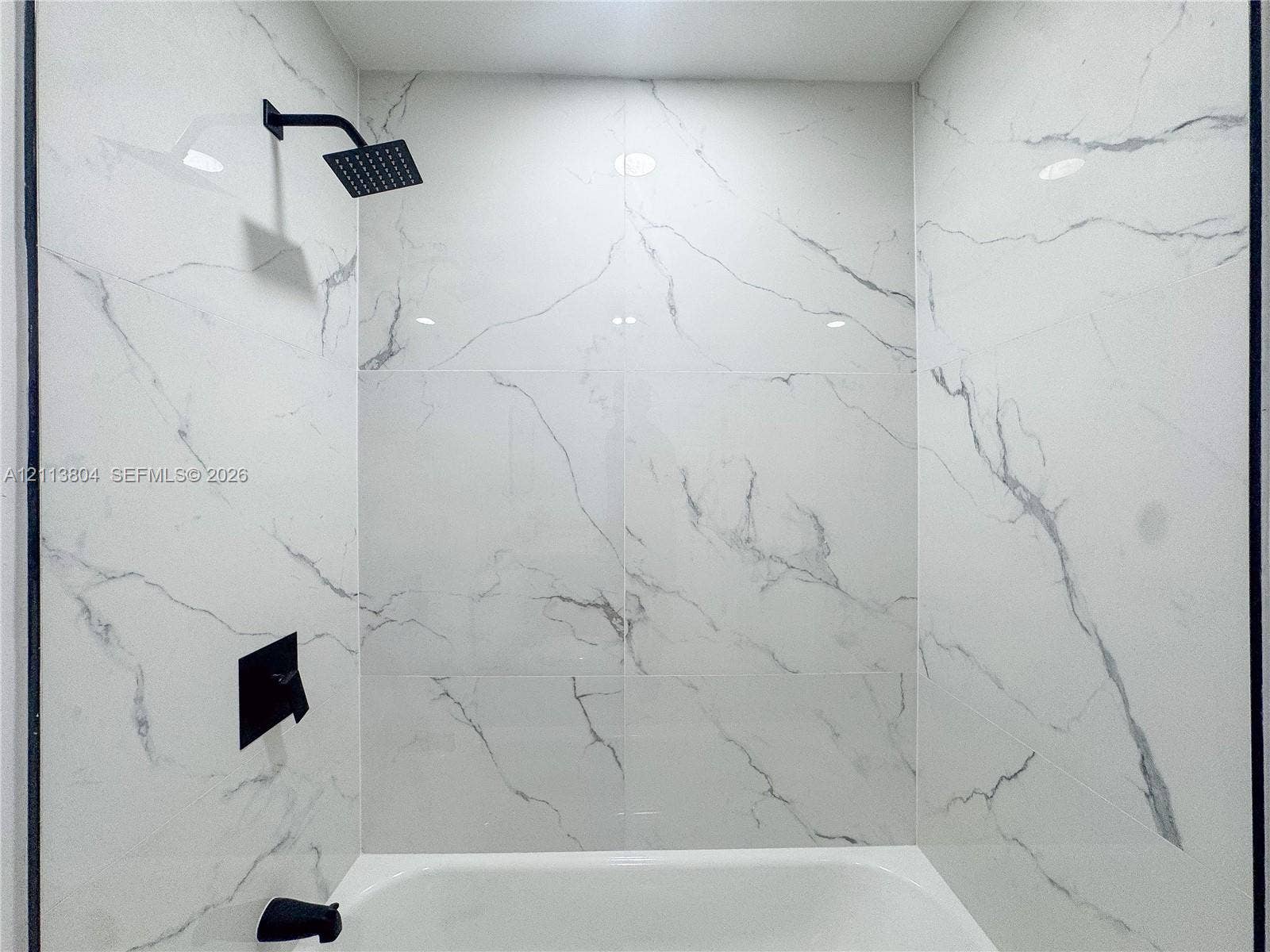 2300 NW 31st Avenue, Fort Lauderdale, FL 33311 Shower area featuring large-format, veined tile wall surround, matte black rainfall showerhead, and matte black wall-mounted faucet controls