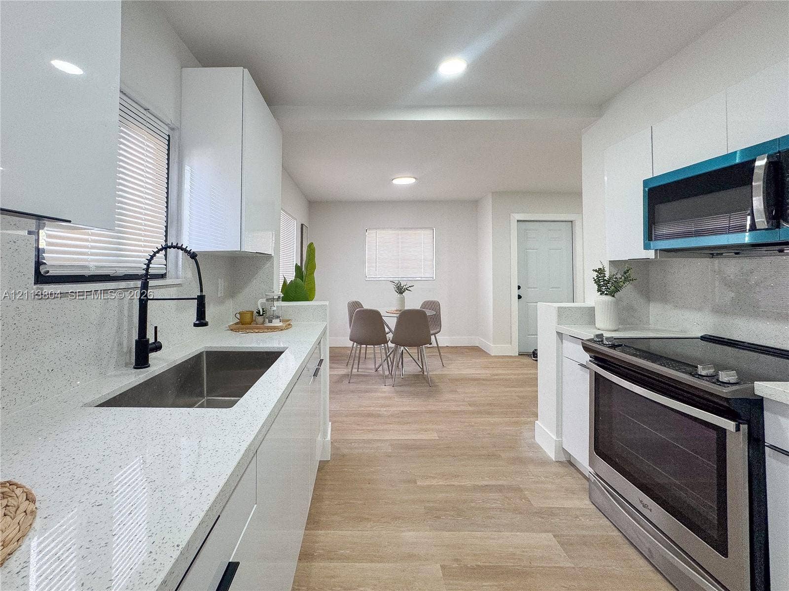 2300 NW 31st Avenue, Fort Lauderdale, FL 33311 Kitchen featuring white slab cabinetry, light-toned stone-finish countertops, stainless steel undermount sink with a matte black faucet, and wood-finish flooring