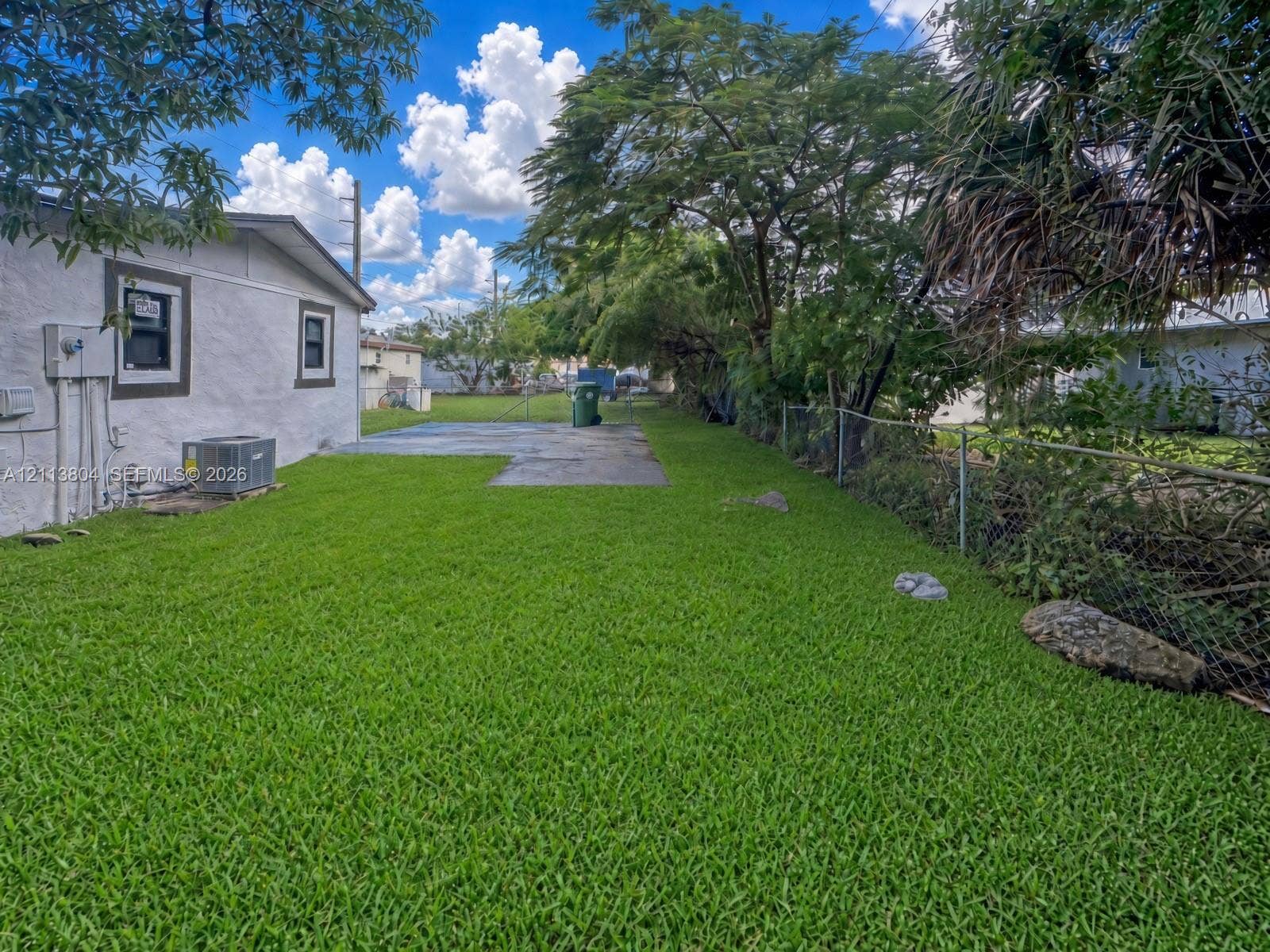 2300 NW 31st Avenue, Fort Lauderdale, FL 33311 Backyard featuring a grass lawn, concrete patio, chain-link fencing, and mature trees
