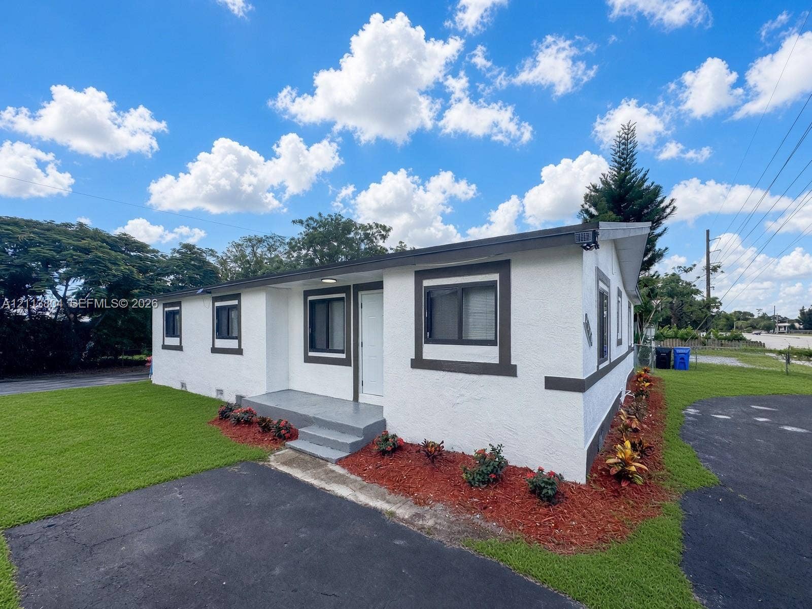 2300 NW 31st Avenue, Fort Lauderdale, FL 33311 Exterior featuring white stucco siding with contrasting trim, a covered concrete front entry, and landscaped perimeter garden beds with mulch